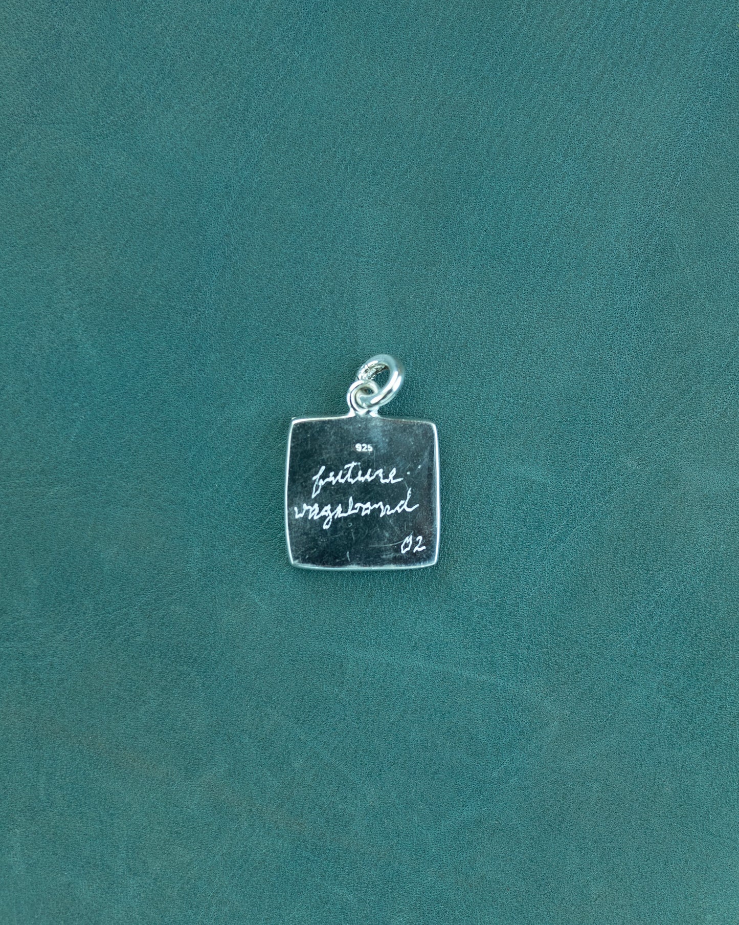 Silver charm with engraved text on a teal background