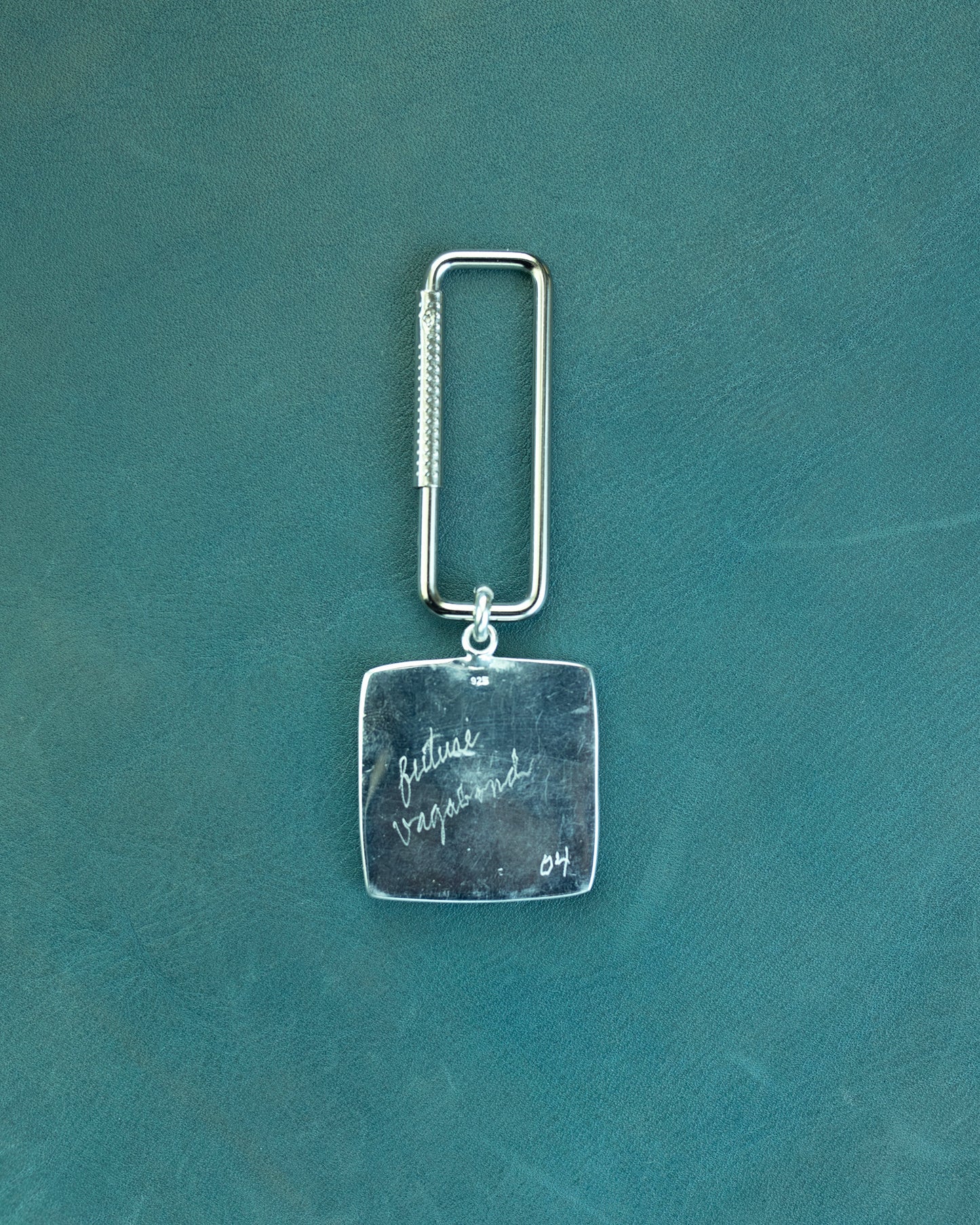 Silver keychain with engraved text on a teal background