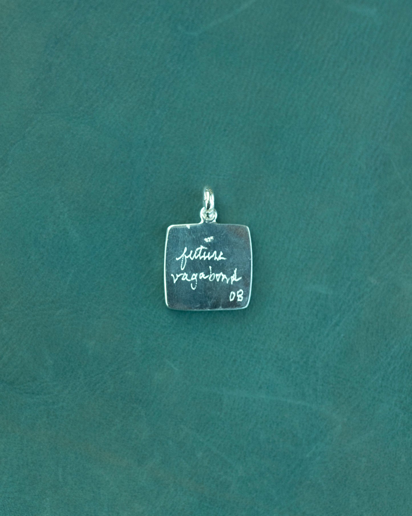 Silver pendant with engraved text on a teal background
