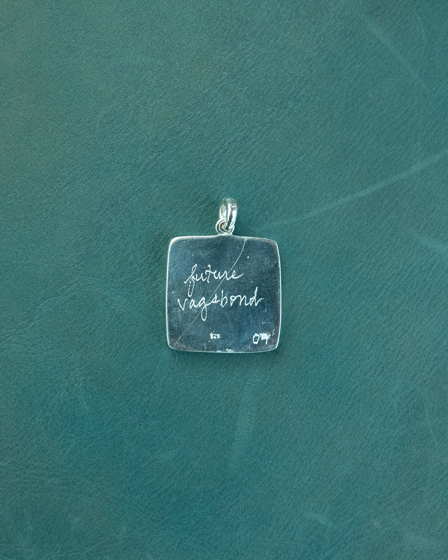 Silver pendant with 'future vagabond' engraving on a green textured background