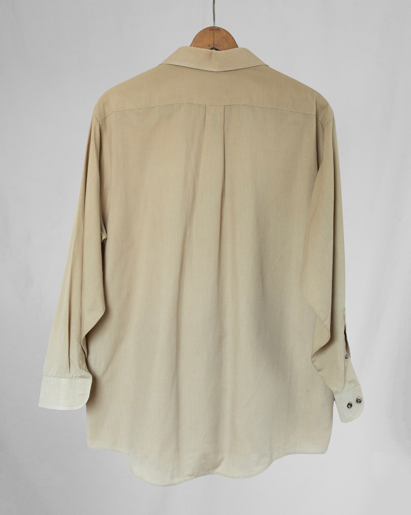Pale yellow shirt on a wooden hanger against a plain background