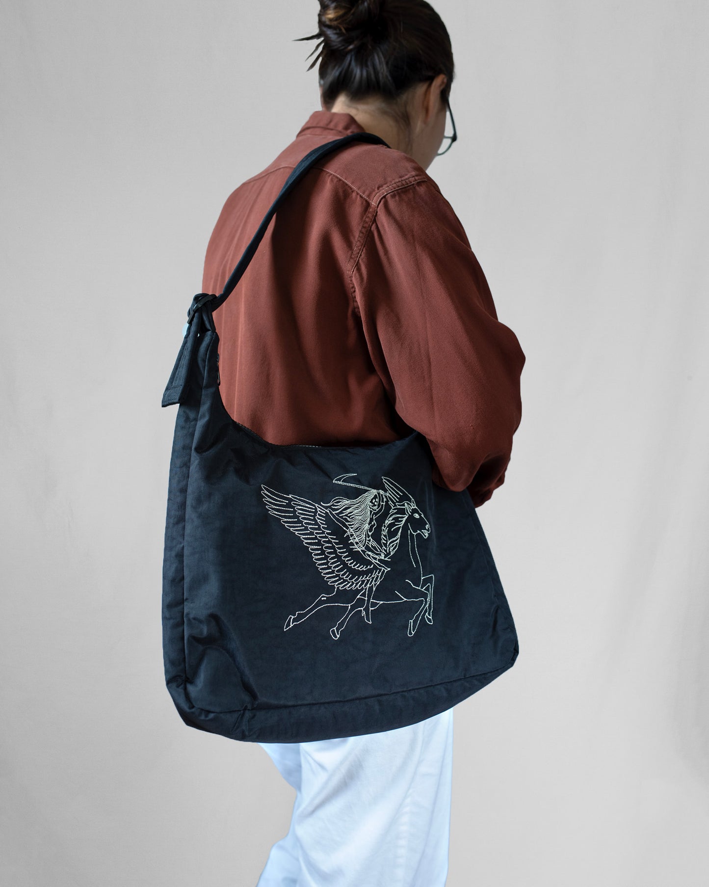 Person wearing a black tote bag with a design, against a plain background