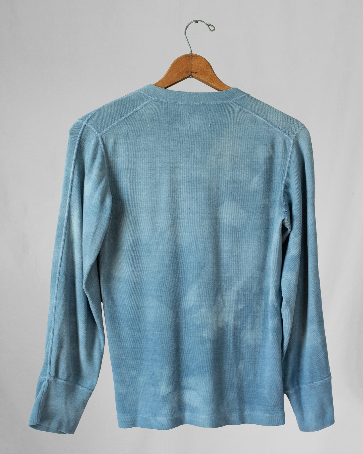 Blue long-sleeve shirt on a hanger against a gray background.