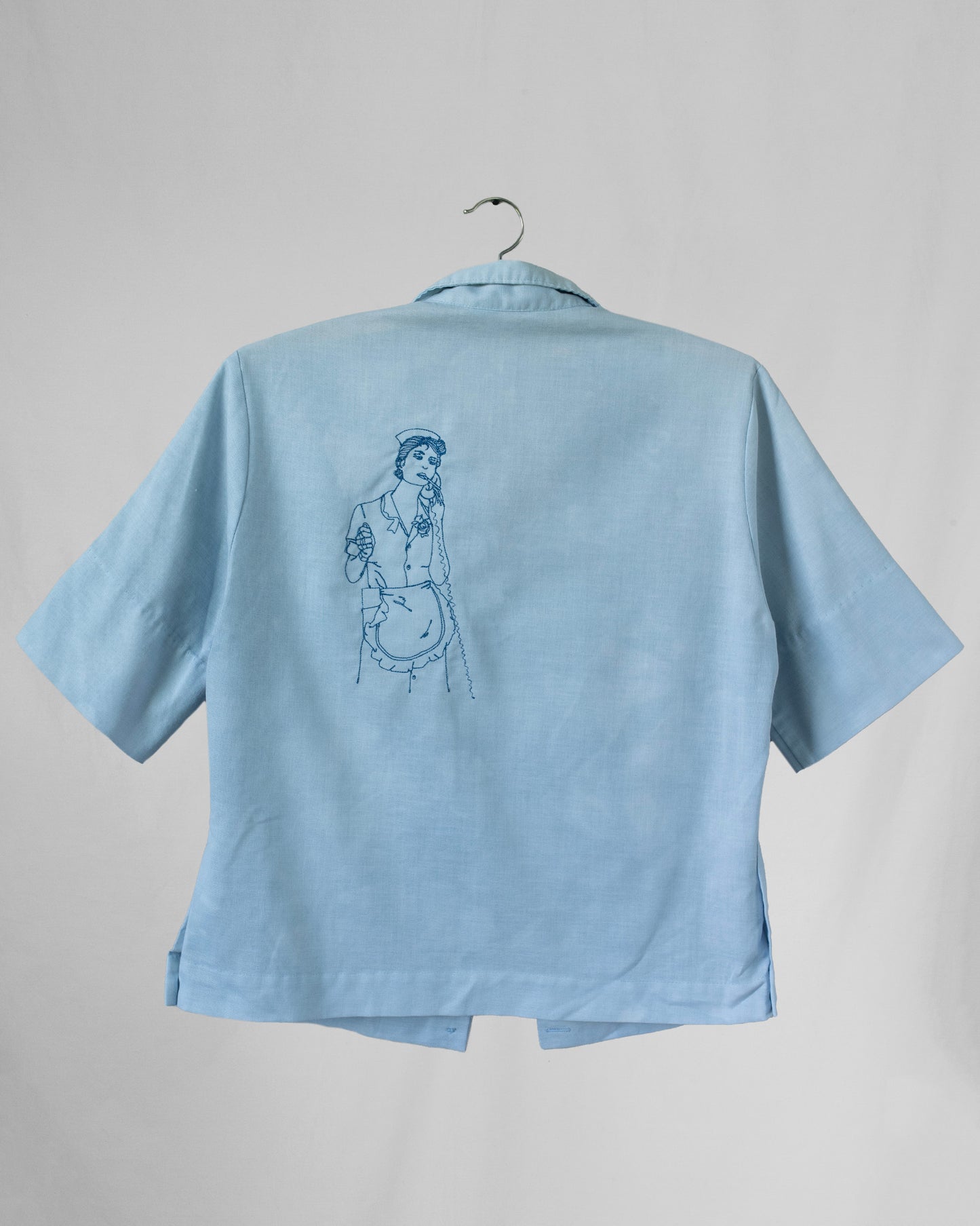 Light blue shirt with an embroidered design on back displayed on a hanger against a gray background