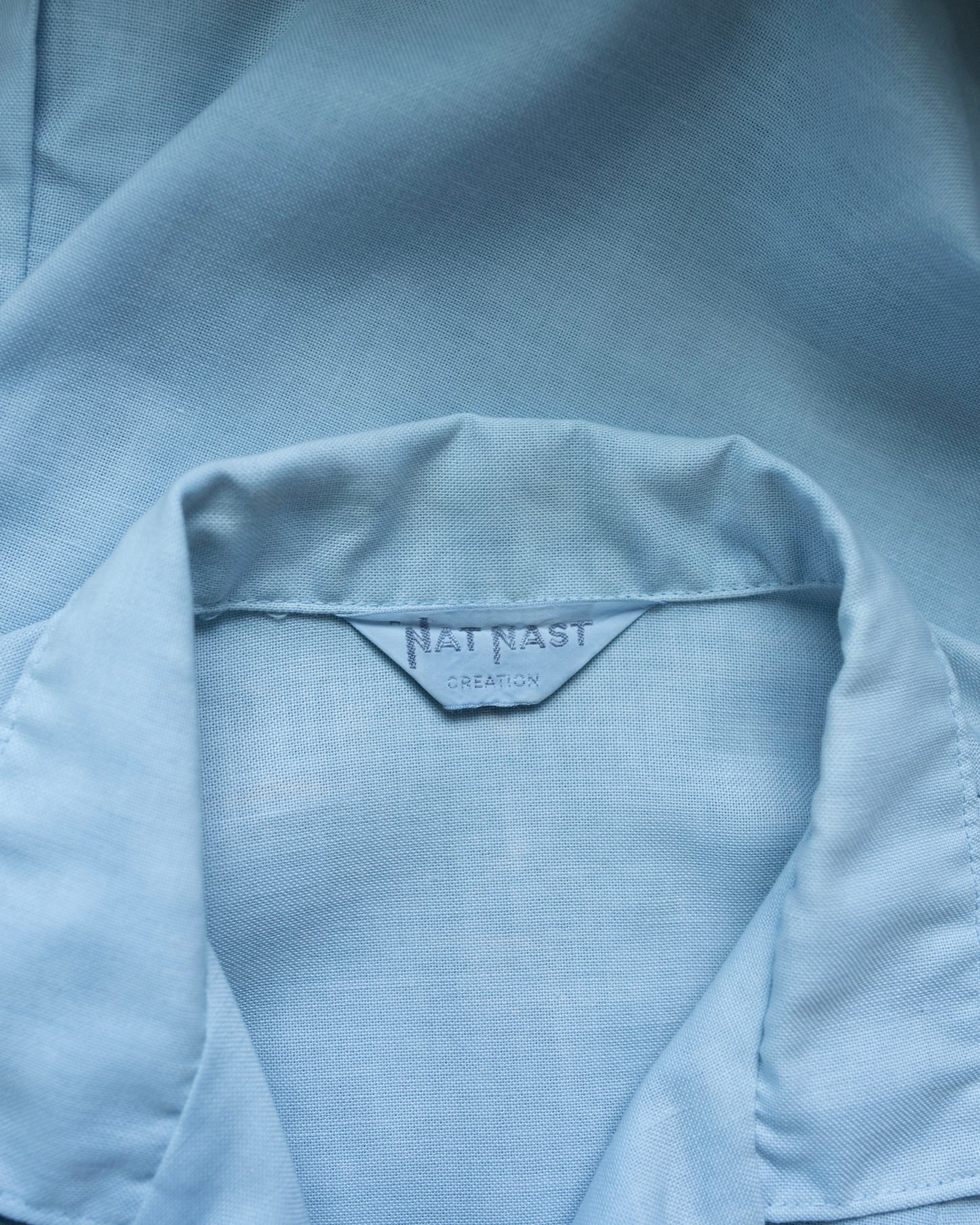 Close-up of a light blue garment with a brand label inside the collar.