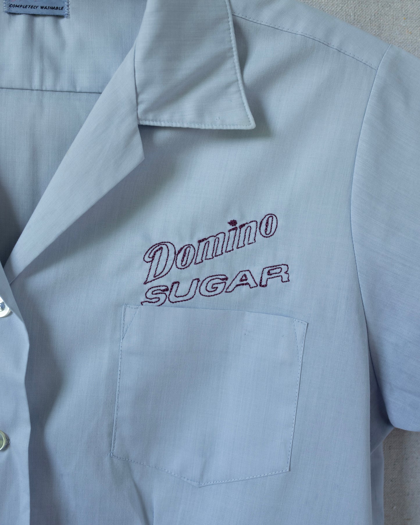 Light blue shirt with 'Domino Sugar' embroidery on a gray background