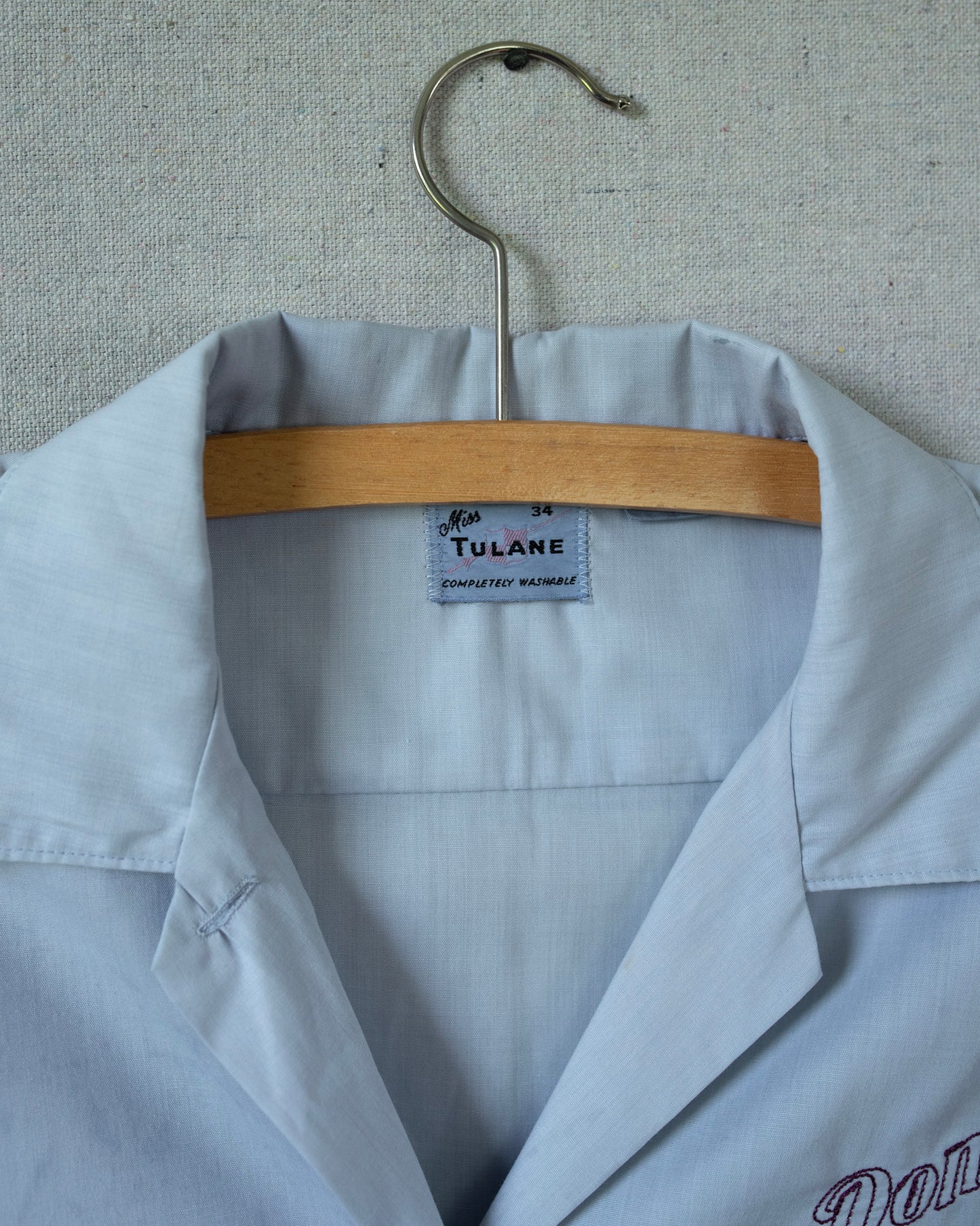 Light blue lab coat with a hanger and 'Tulane' label on a textured background