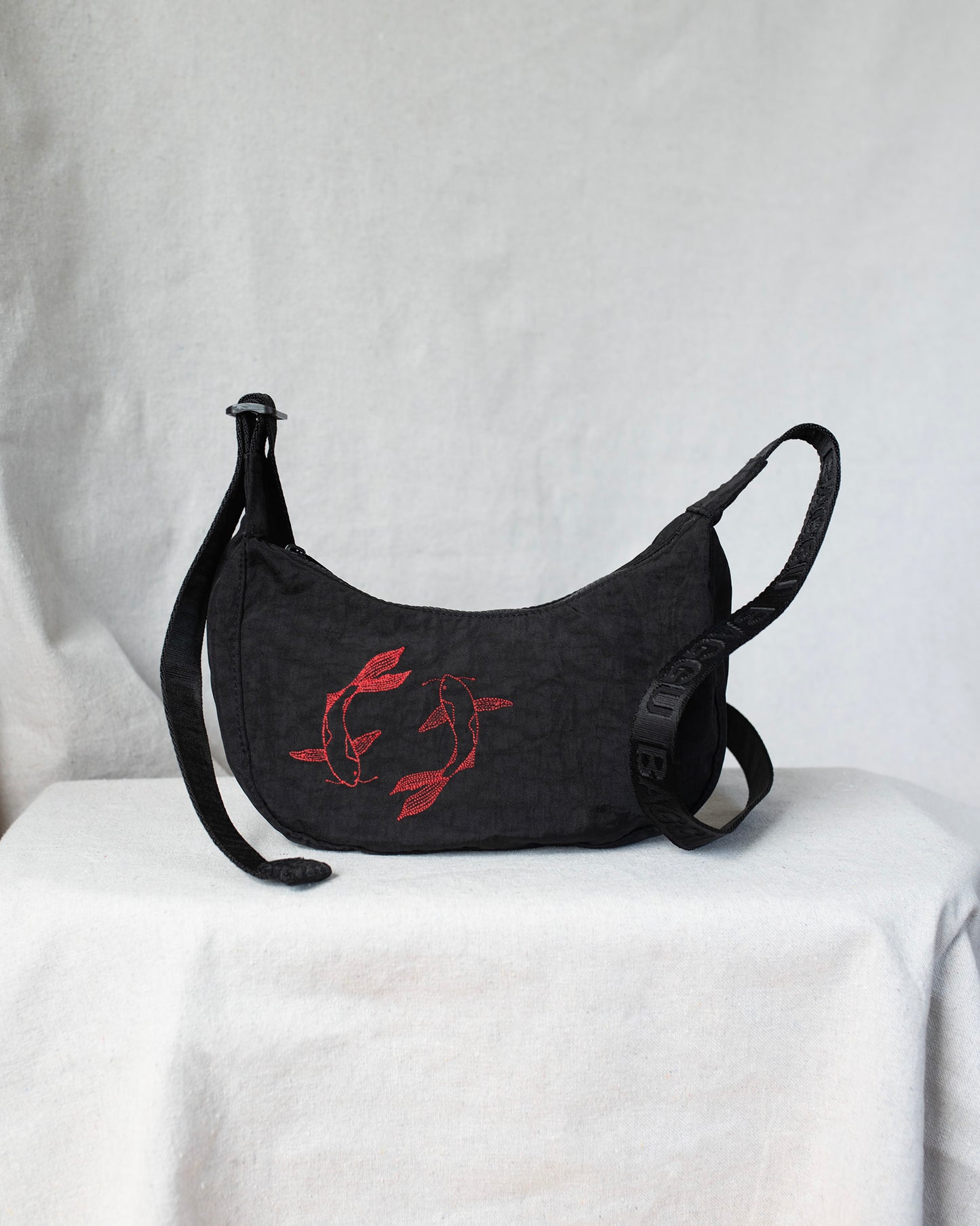 Black crossbody bag with red fish embroideries on a white surface