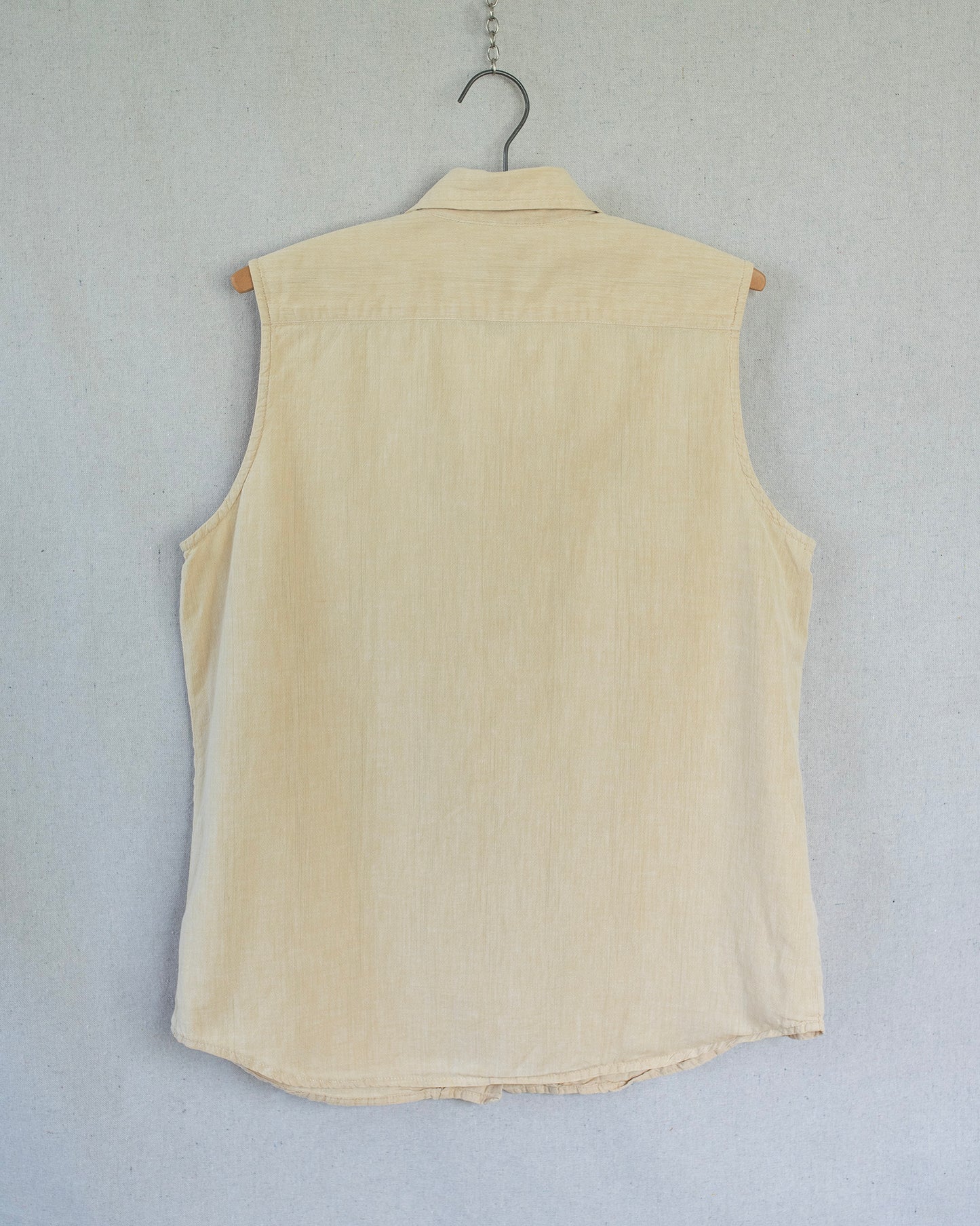 Yellow sleeveless shirt on a hanger against a light gray background