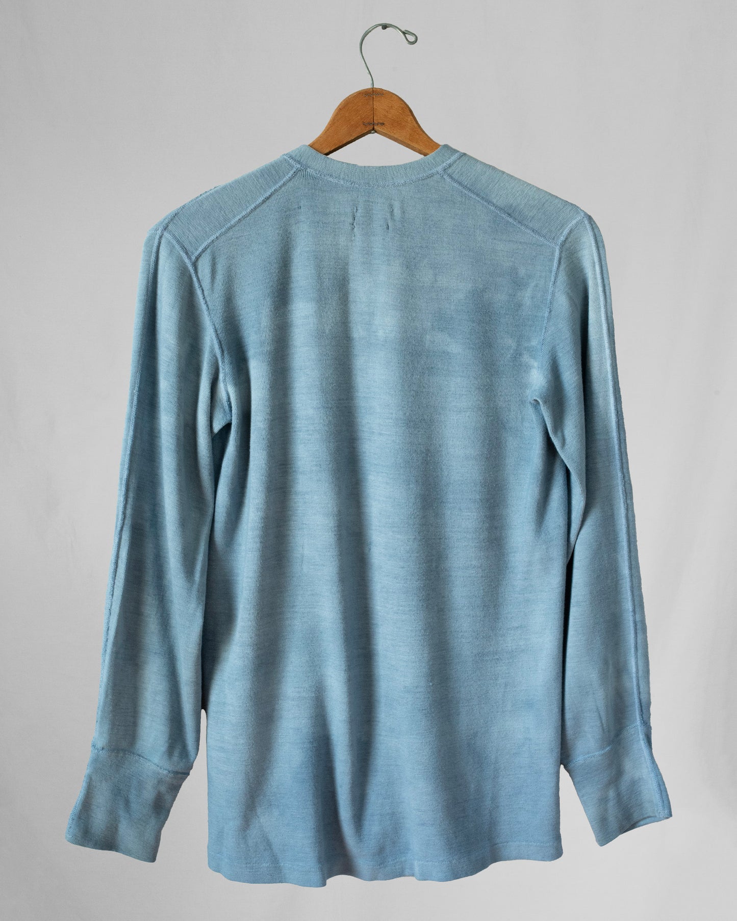 Blue long-sleeve shirt on a wooden hanger against a gray background