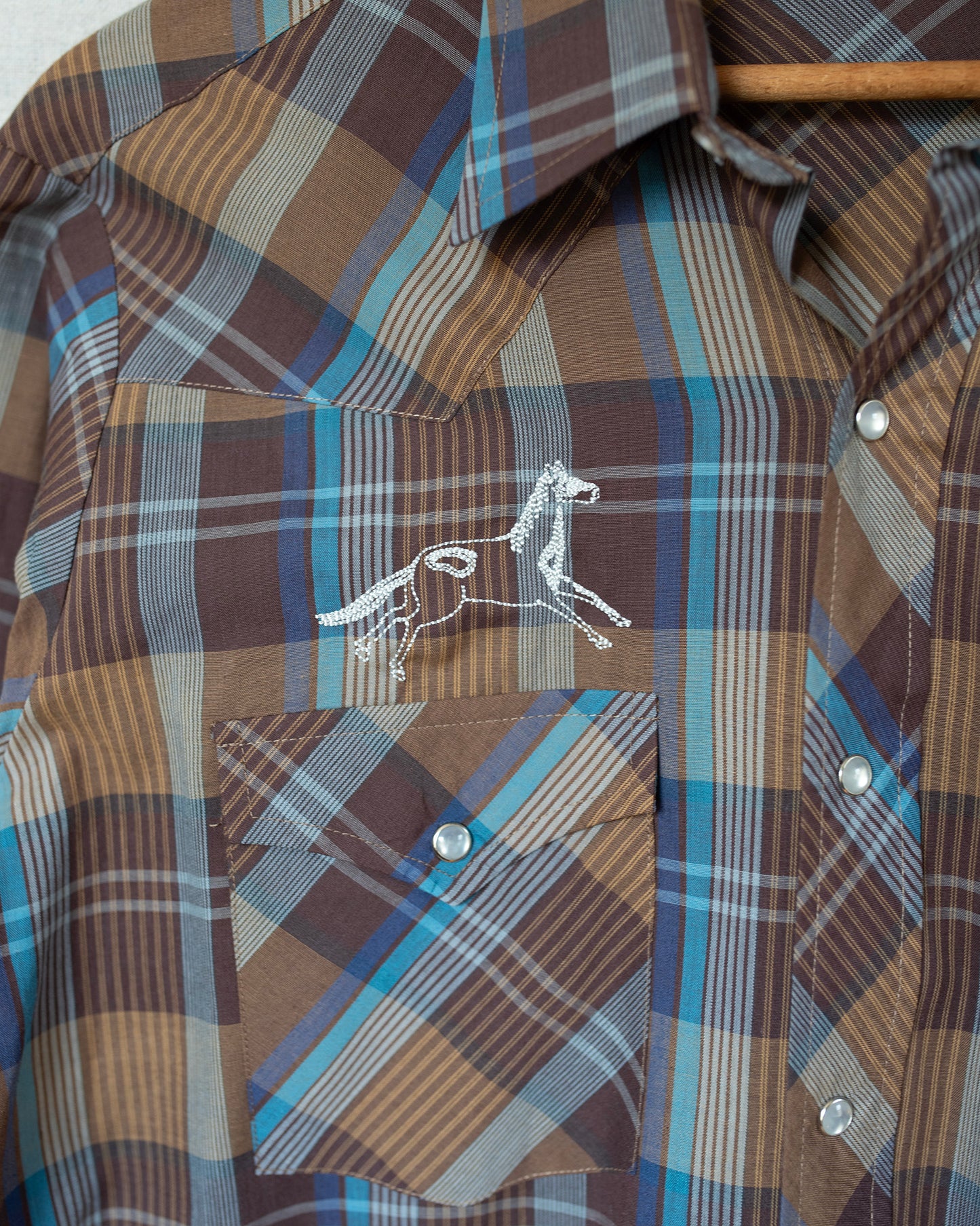 Plaid pearl snap with detail of horse embroidery.