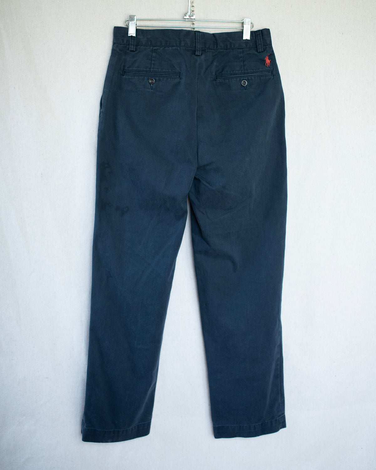 Dark navy trousers hanging on a metal hanger against a light background.