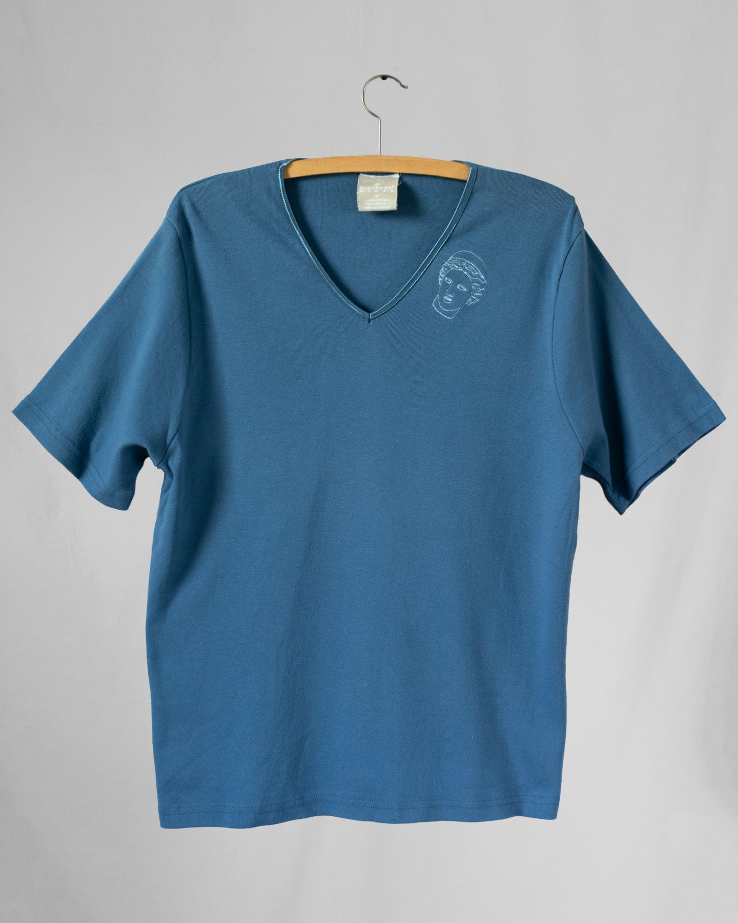 Blue t-shirt with a small embroidery on a hanger against a gray background