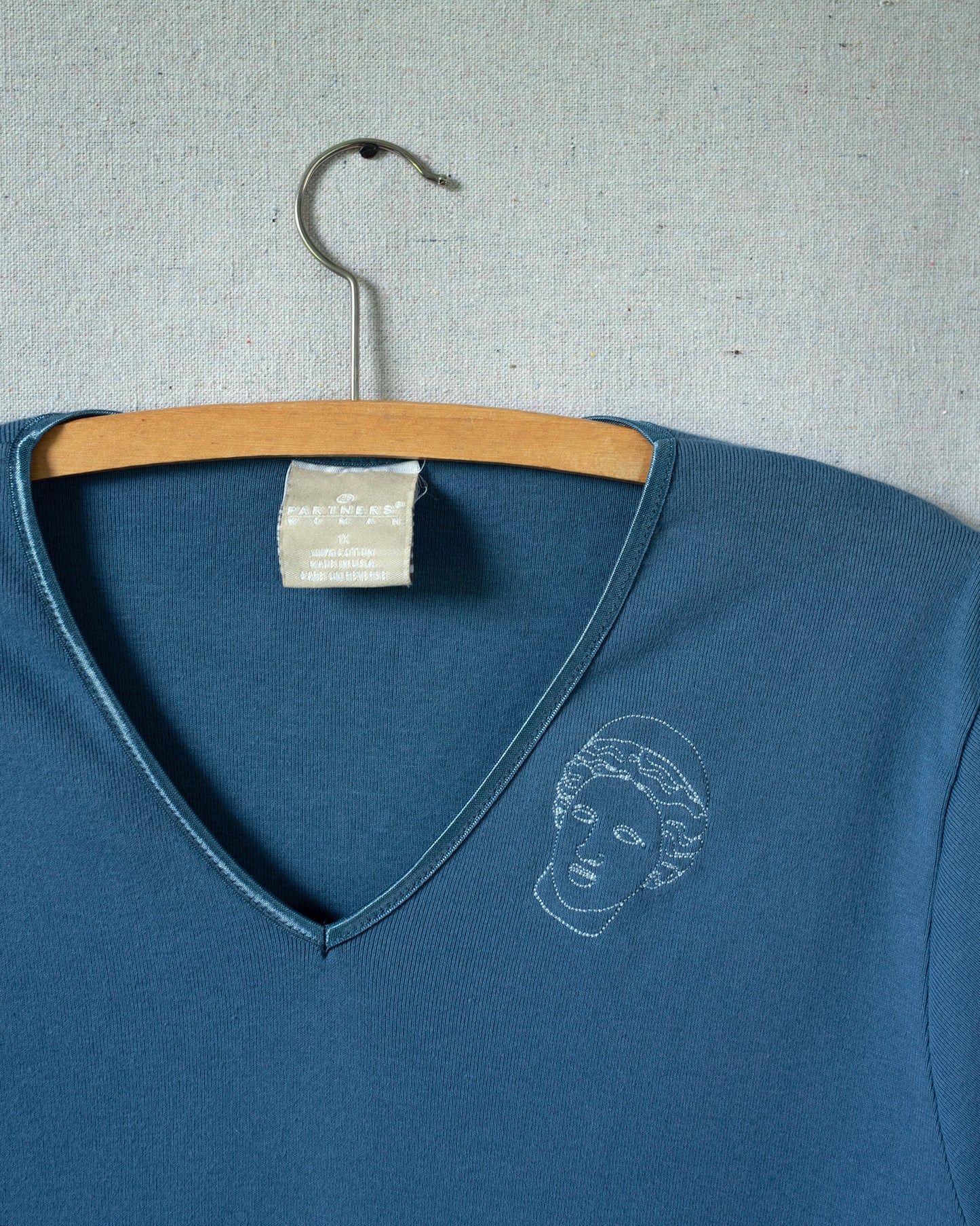 Blue V-neck shirt with a white graphic on a hanger against a gray background