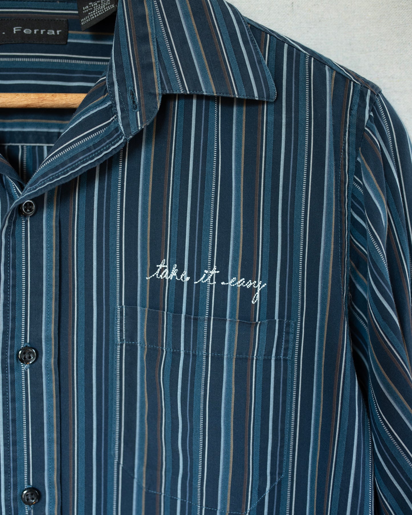 Blue striped shirt with 'take it easy' embroidery on a gray background