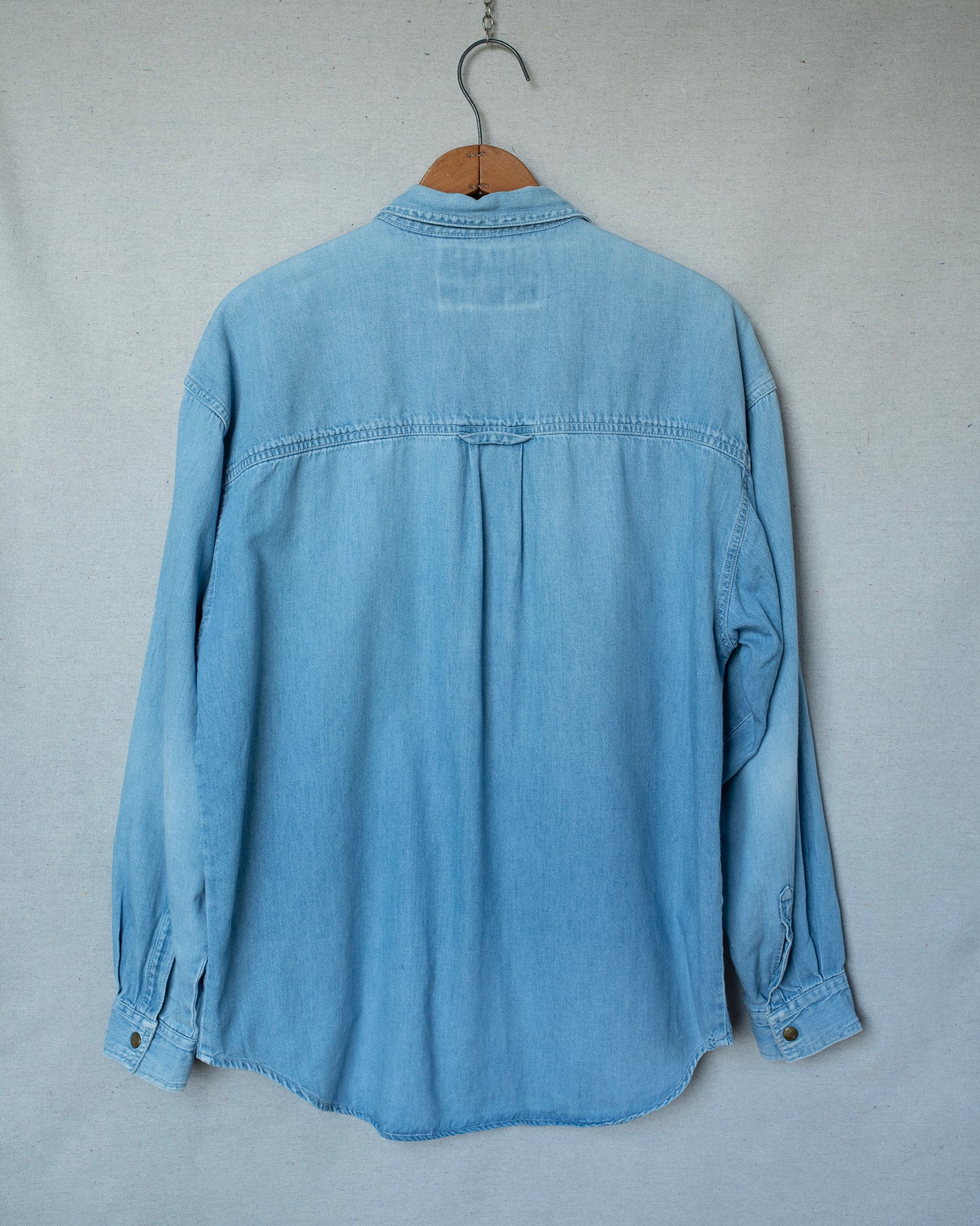 Light blue denim shirt on a hanger against a gray background