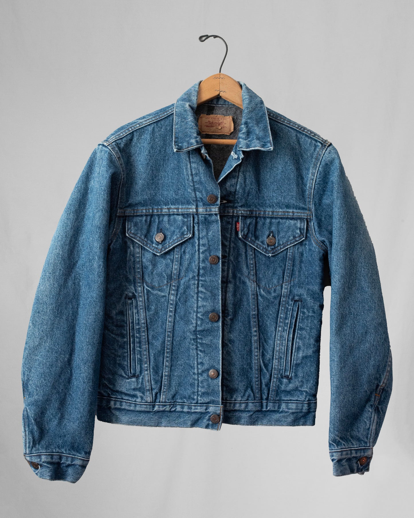 Blue denim jacket on a hanger against a gray background
