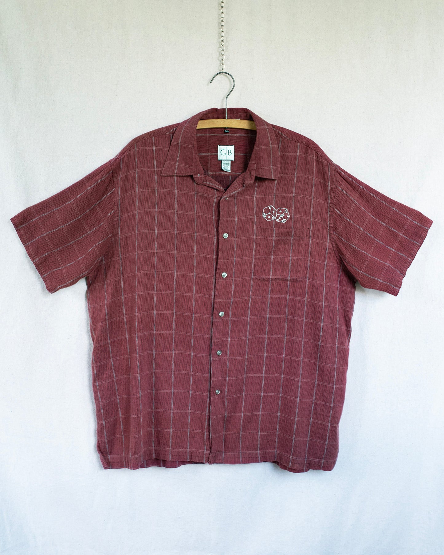Maroon checkered shirt with a dice embroidery on a hanger against a white background