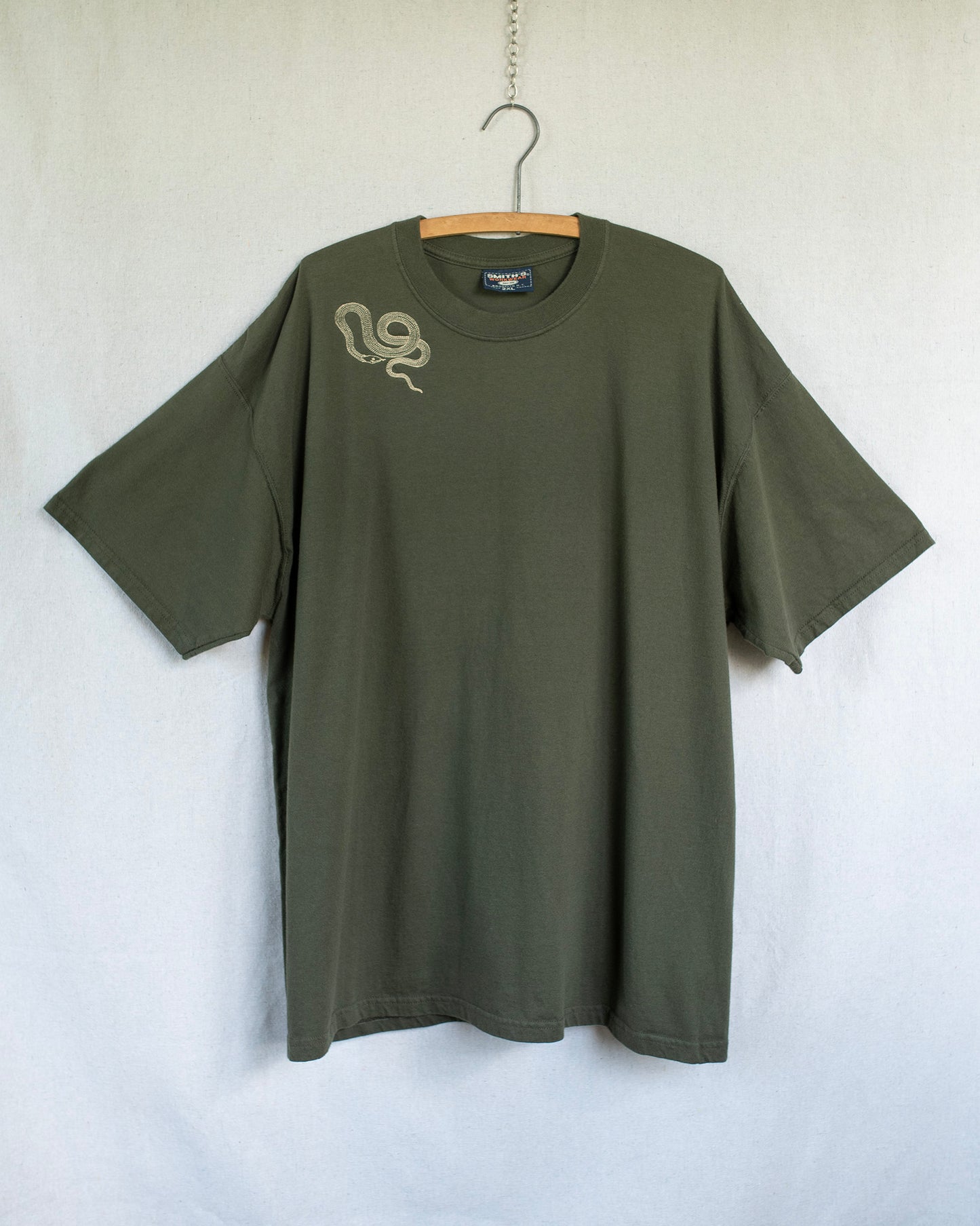 Green t-shirt with a snake embroidery on a hanger against a white background