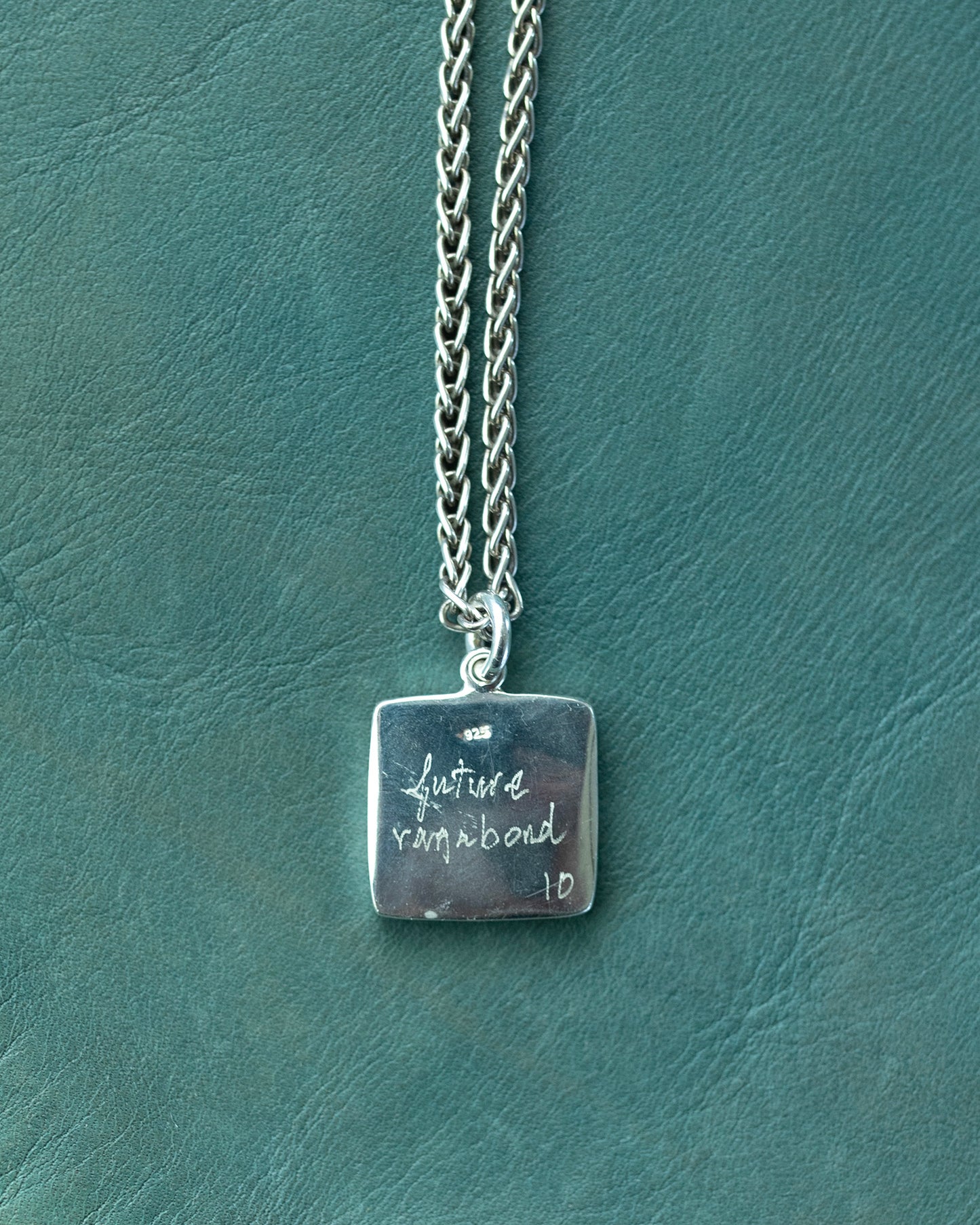 Silver necklace with a square pendant on a textured green surface