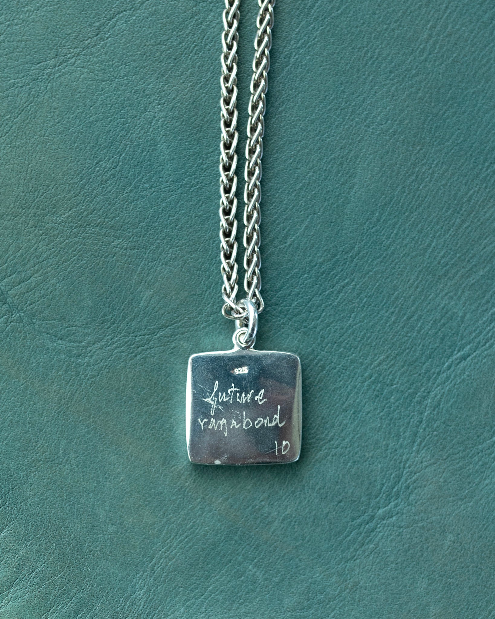Silver necklace with a square pendant on a textured green surface