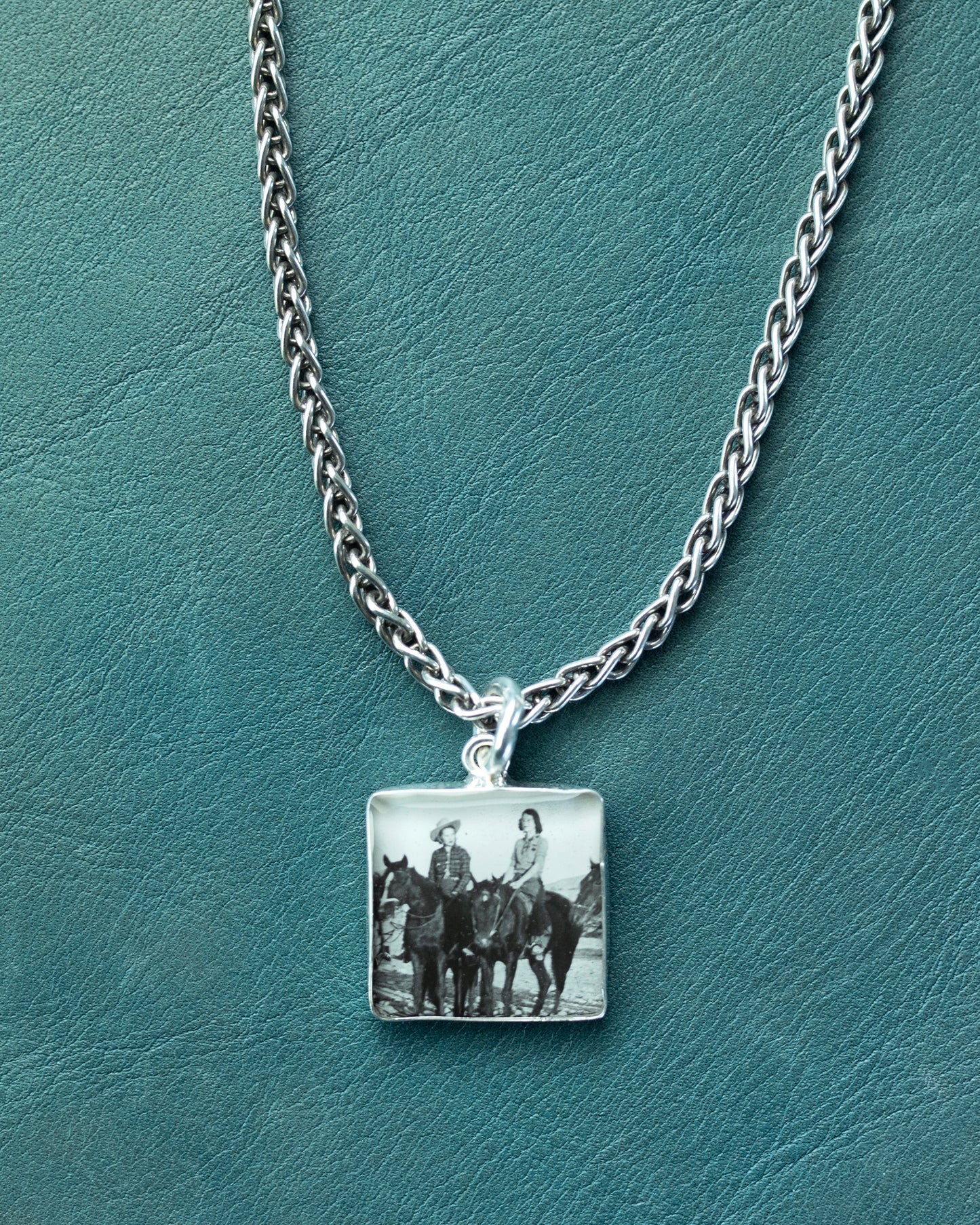 Necklace with a square pendant featuring an image of people on horses on a teal background