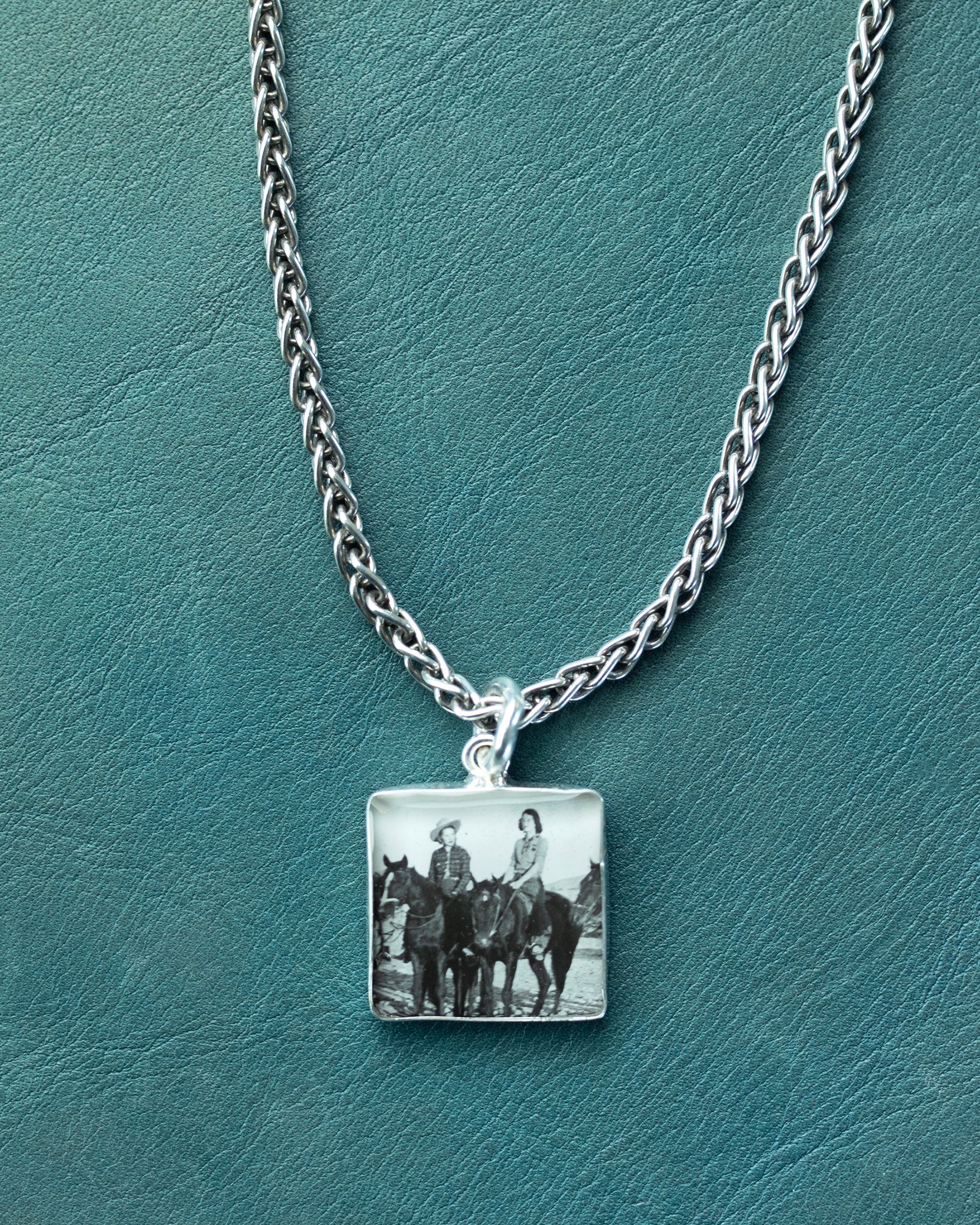 Necklace with a square pendant featuring an image of people on horses on a teal background