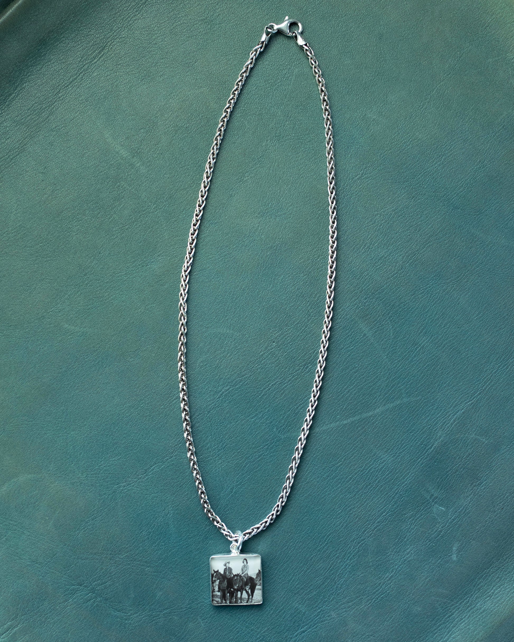 Silver chain necklace with a square pendant on a green textured surface