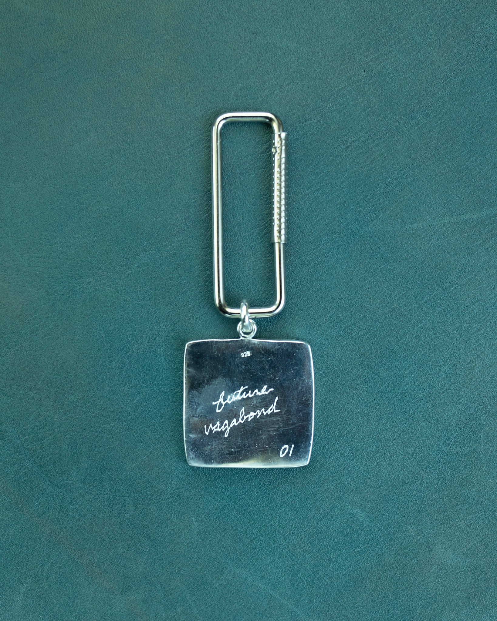 Silver keychain with engraved text on a teal background