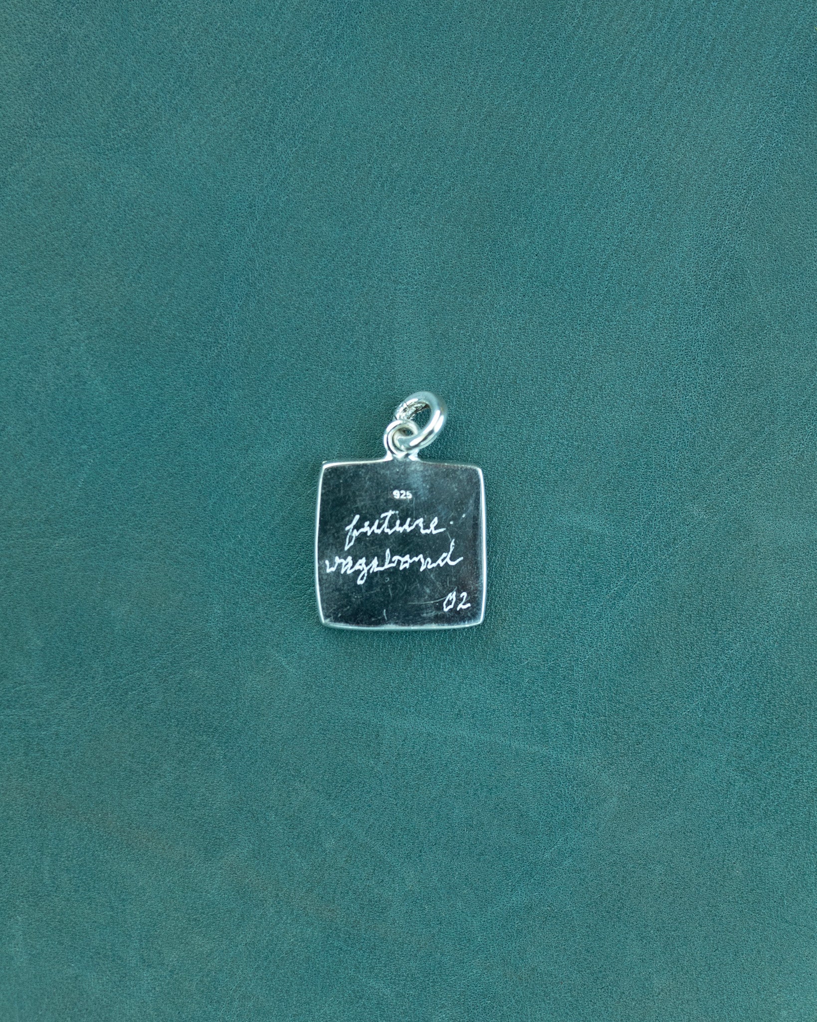 Silver charm with engraved text on a teal background