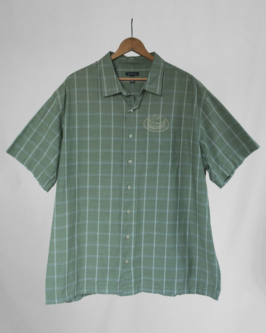 Green checkered shirt with pancakes embroidered above the chest pocket on a hanger against a plain background