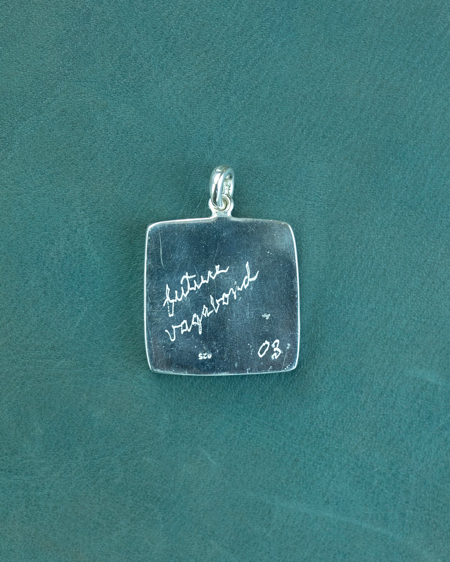 Silver pendant with engraved text on a teal background
