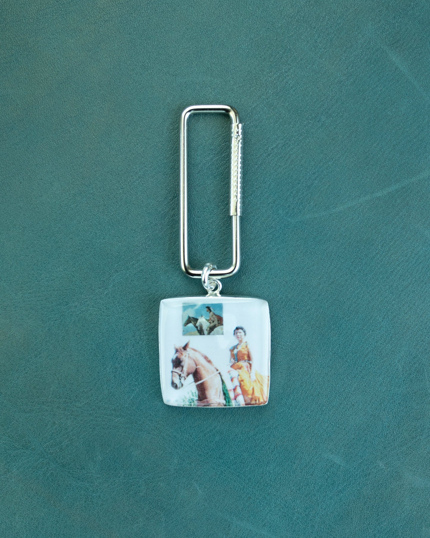 Keychain with a square pendant featuring images of a horse and rider on a green background