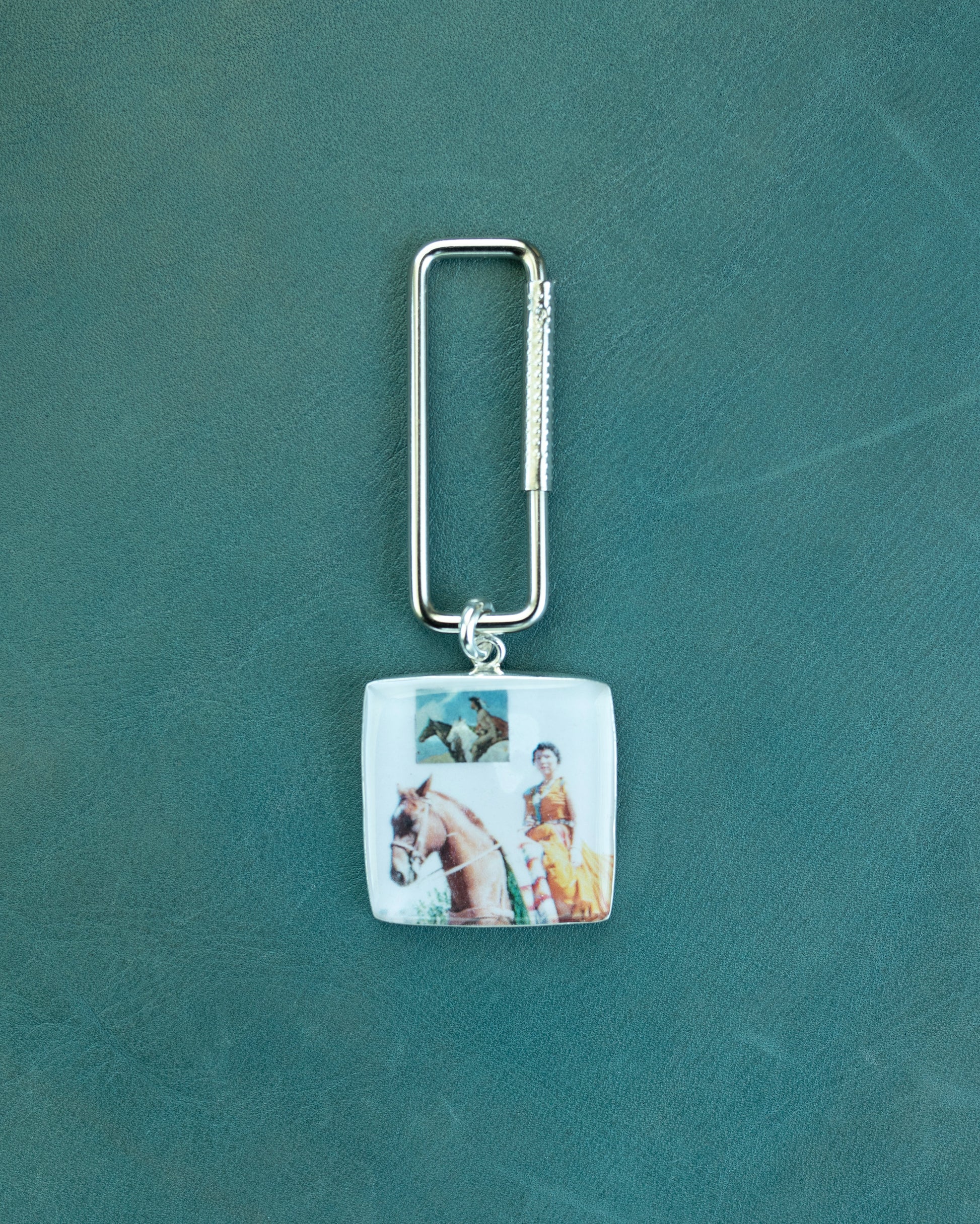 Keychain with a square pendant featuring images of a horse and rider on a green background