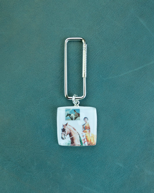 Keychain with a square pendant featuring images of a horse and rider on a green background