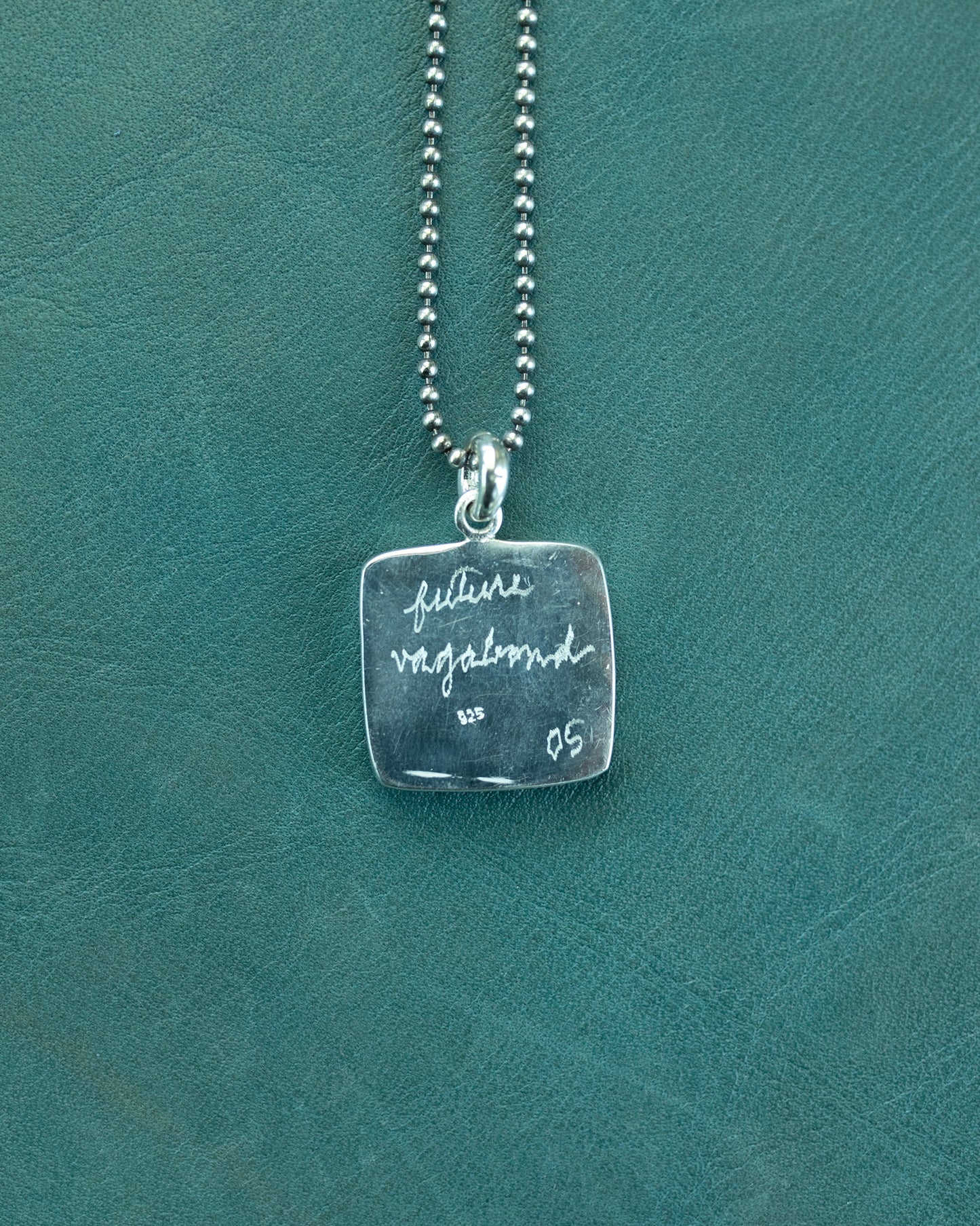 Silver necklace with a square pendant on a teal background