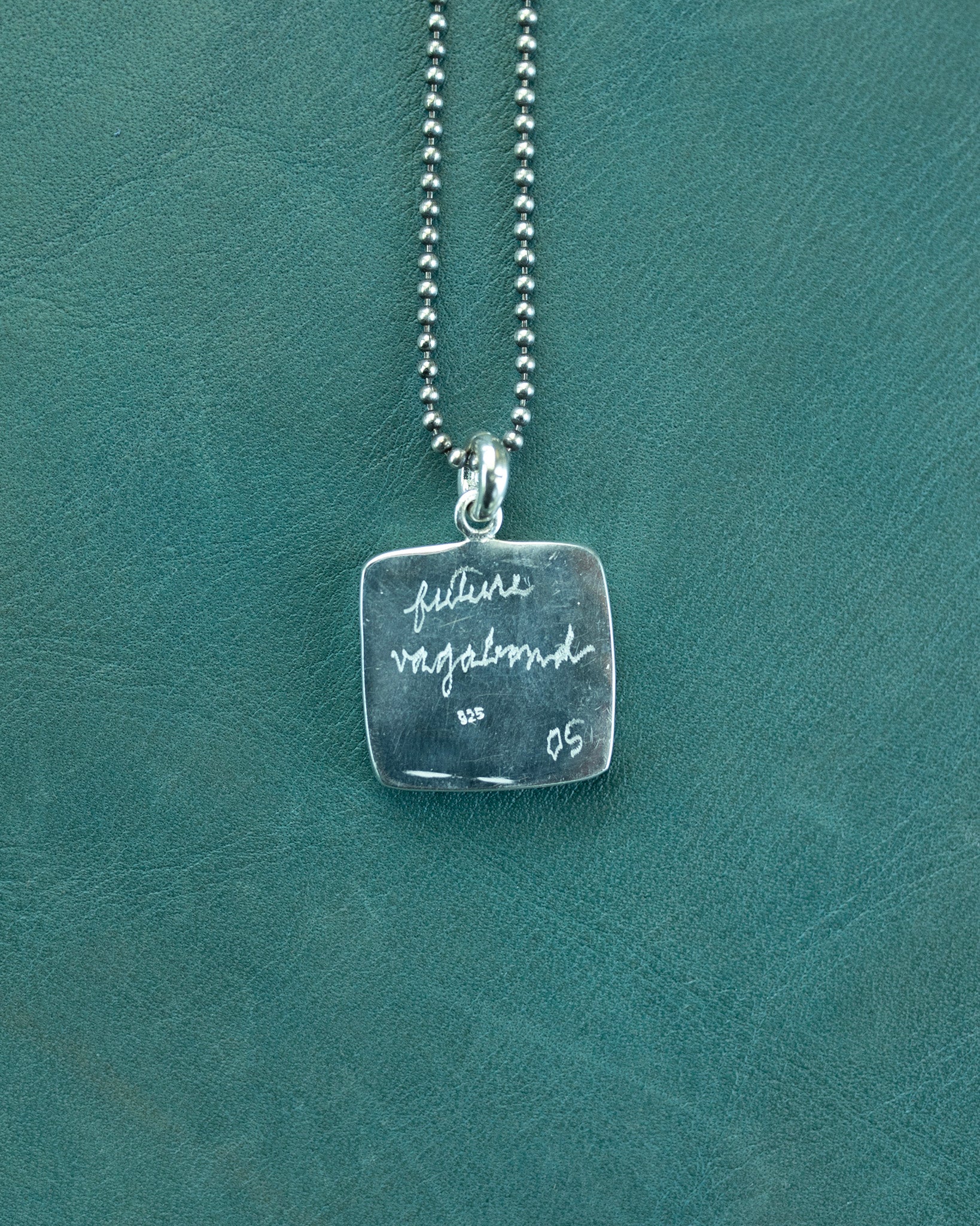 Silver necklace with a square pendant on a teal background