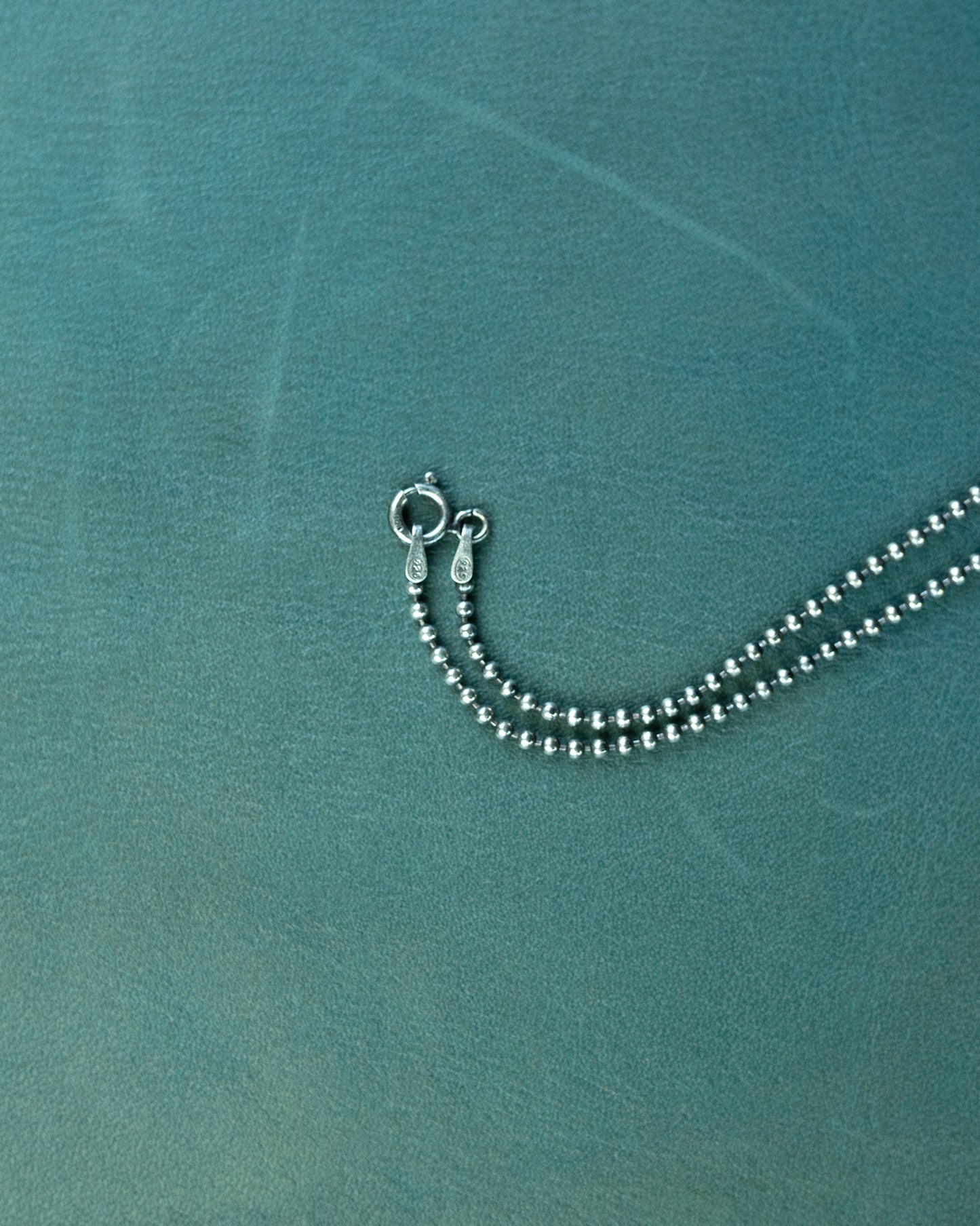 Silver beaded necklace on a textured teal surface