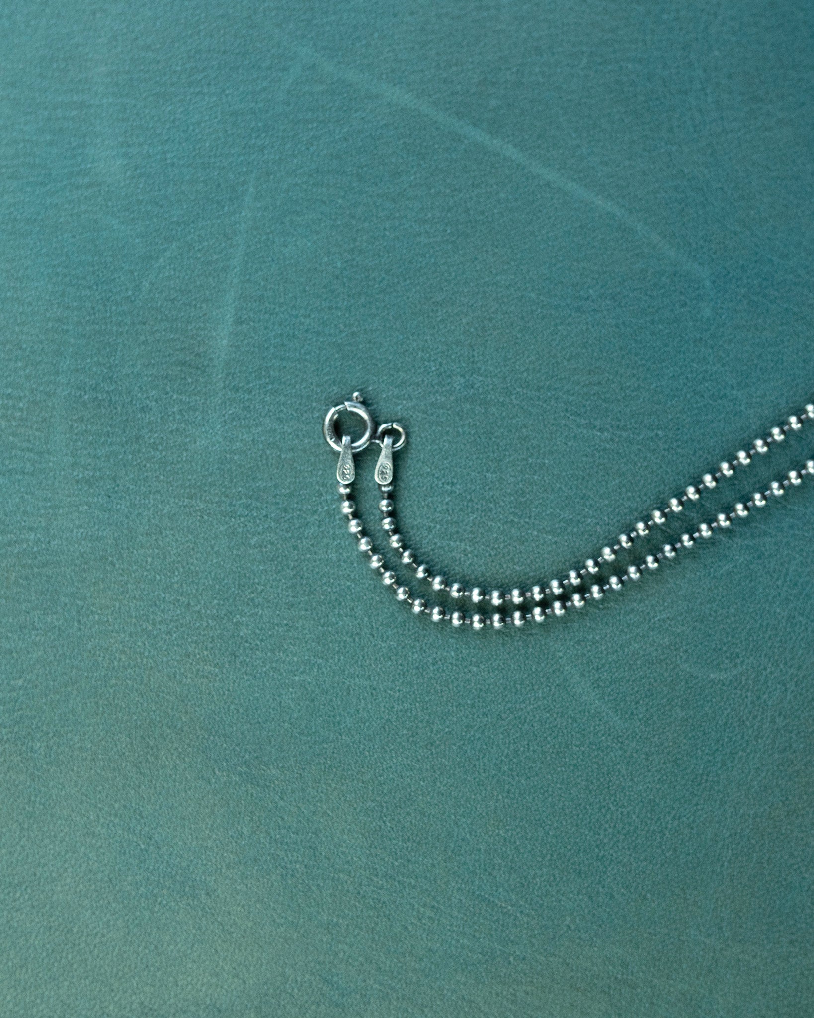 Silver beaded necklace on a textured teal surface