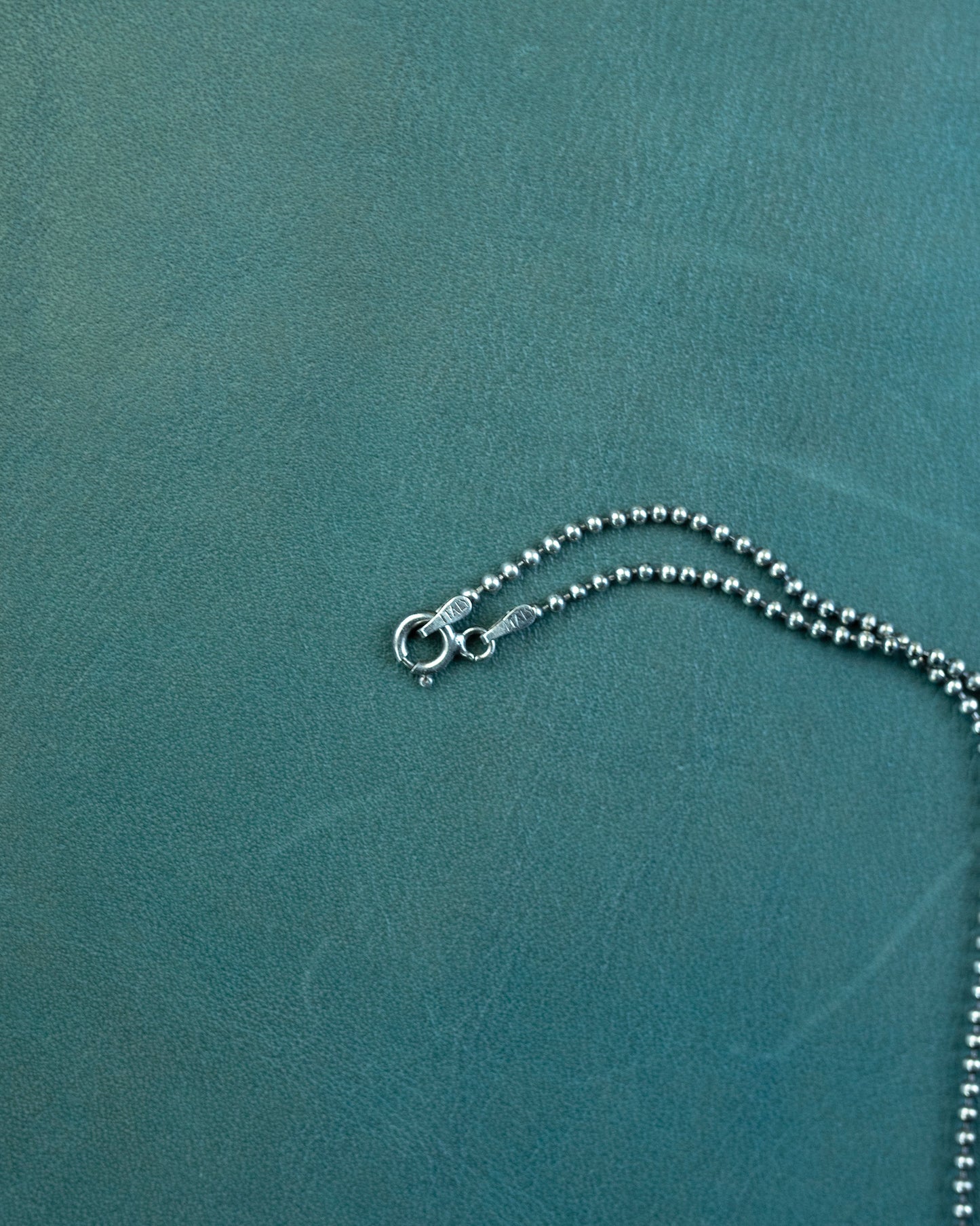 Silver necklace on a textured teal background
