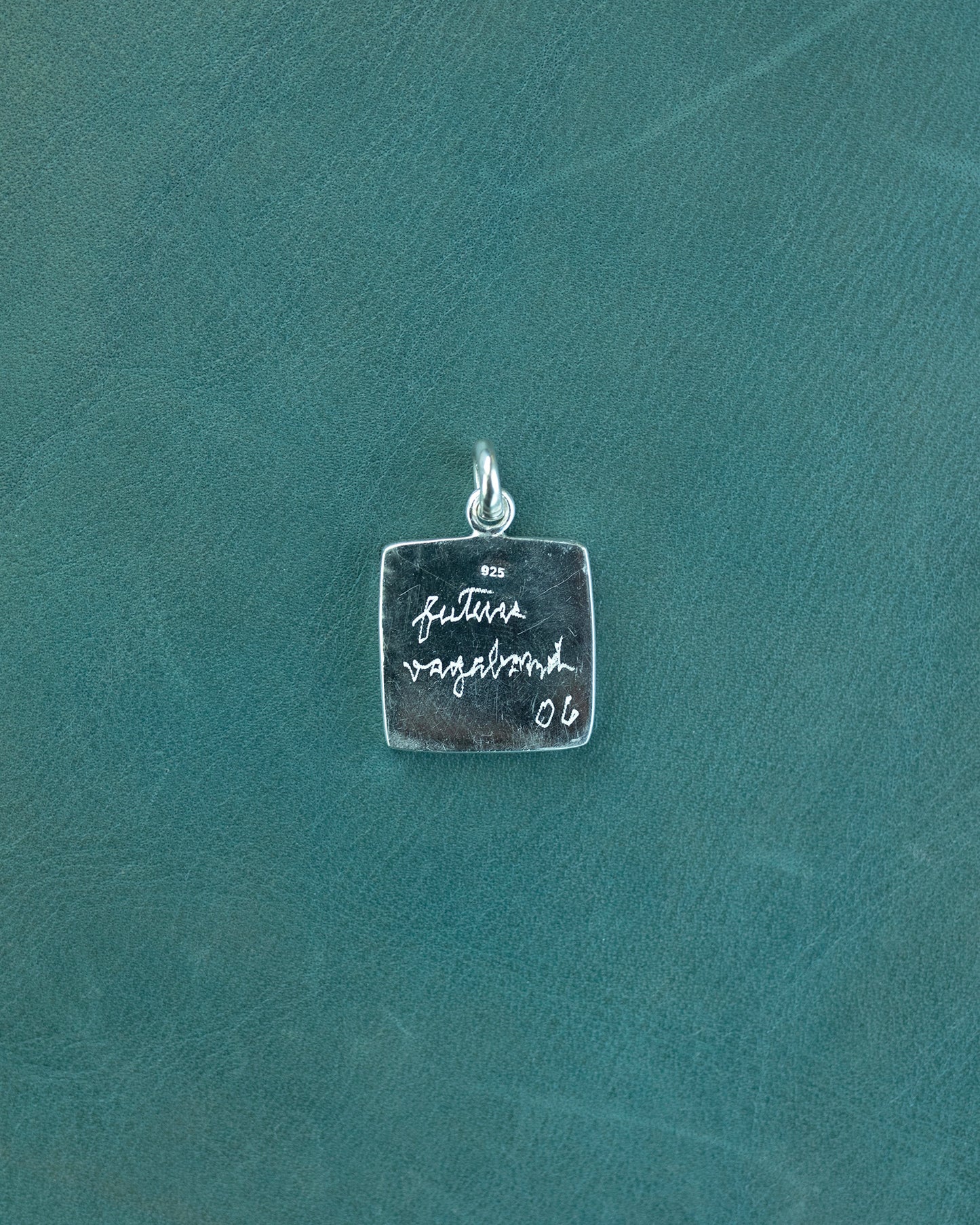 Silver pendant with engraved text on a teal background