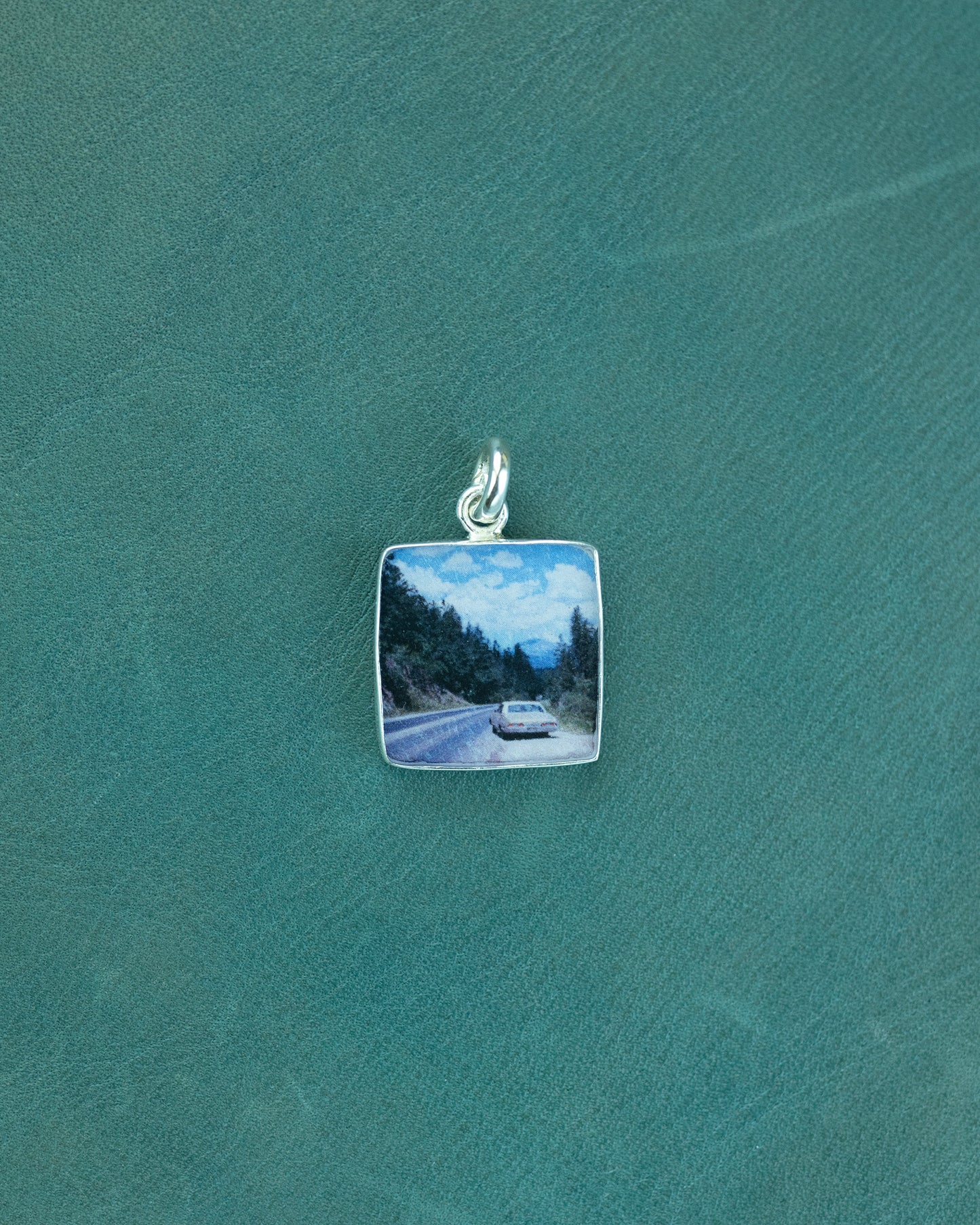 Silver pendant with a scenic road and car design on a green background