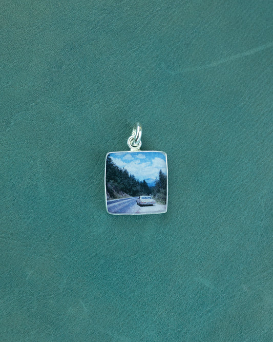 Silver pendant with a scenic road and car design on a green background