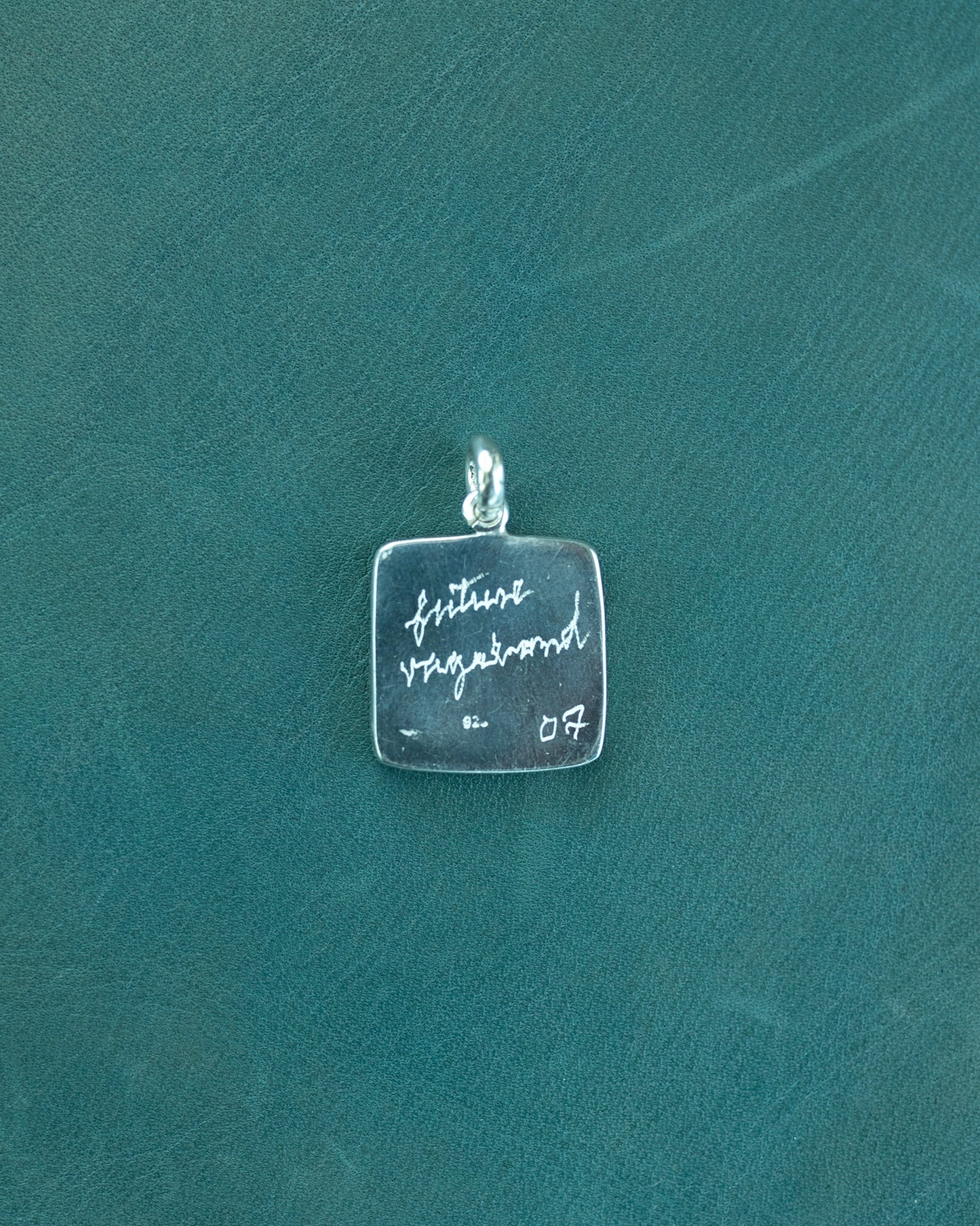 Silver pendant with engraved text on a teal background