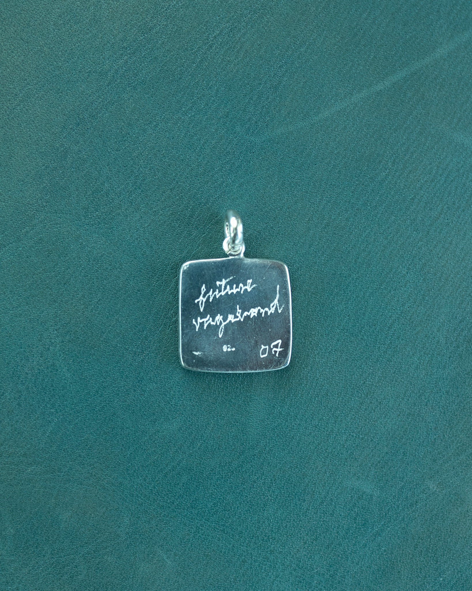 Silver pendant with engraved text on a teal background