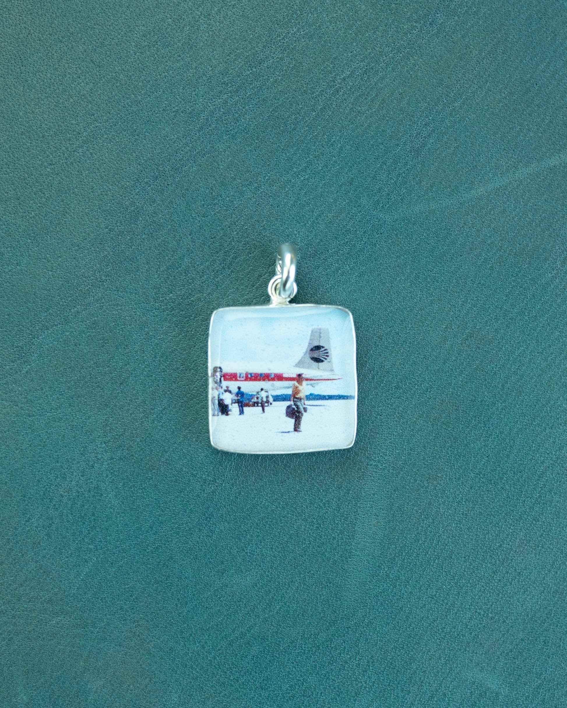 Square pendant with a part of a plane and people walking on a green background