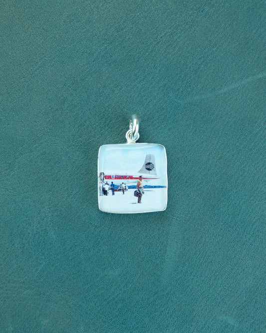 Square pendant with a part of a plane and people walking on a green background