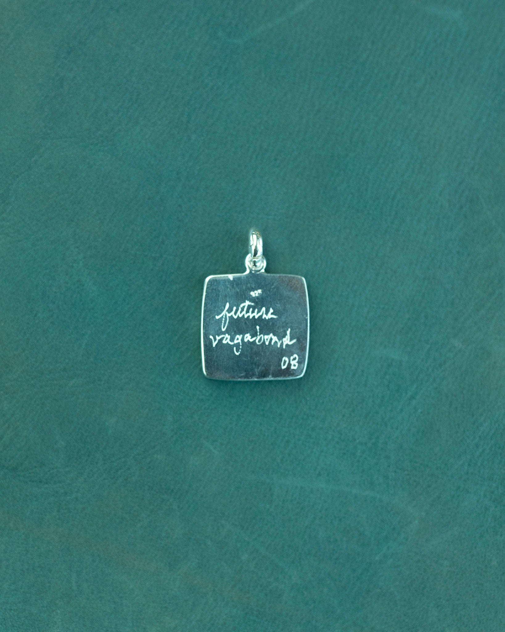 Silver pendant with engraved text on a teal background