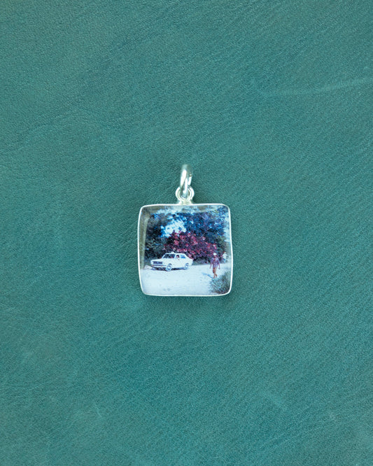 Silver pendant with a scenic engraving on a green textured background