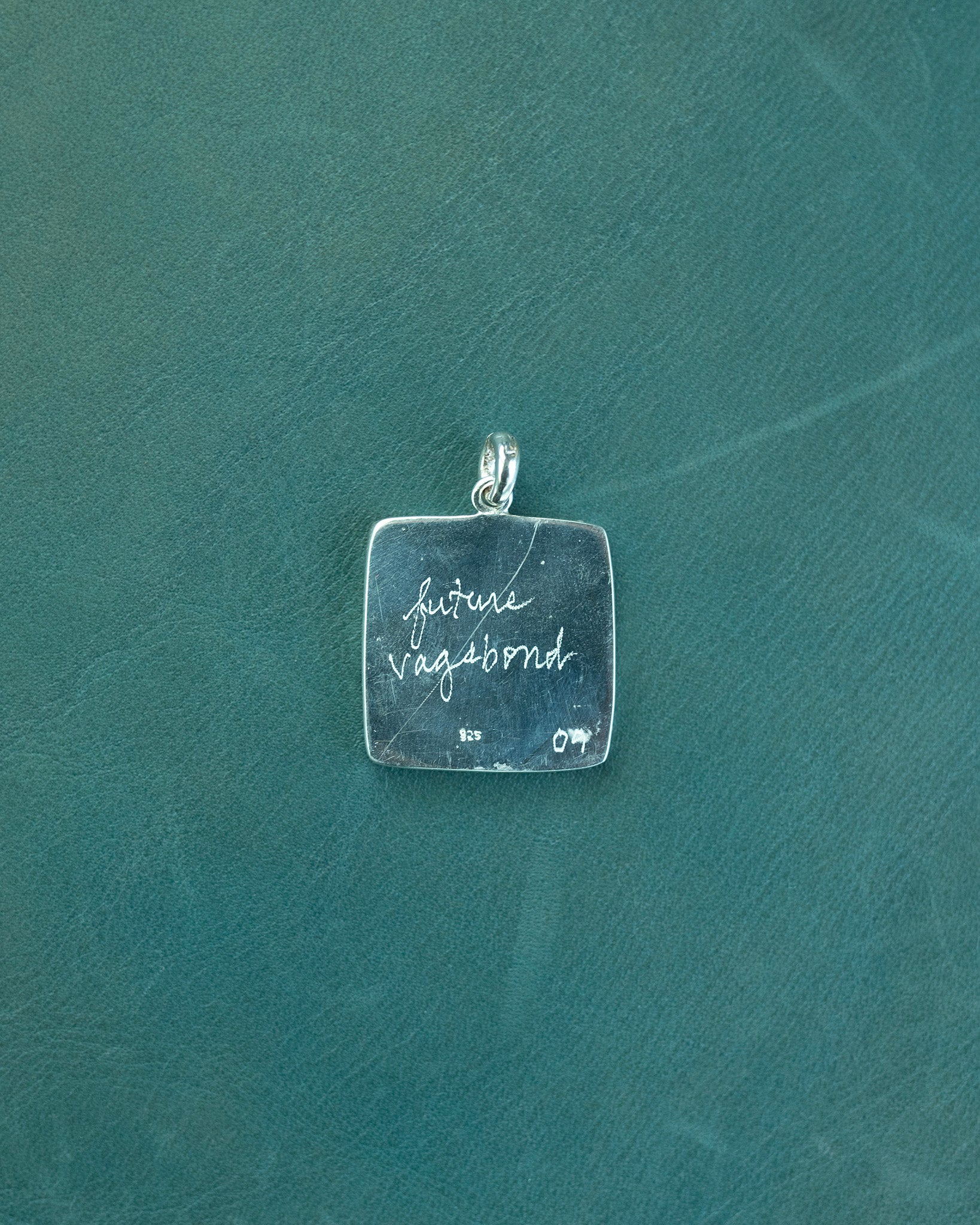 Silver pendant with 'future vagabond' engraving on a green textured background